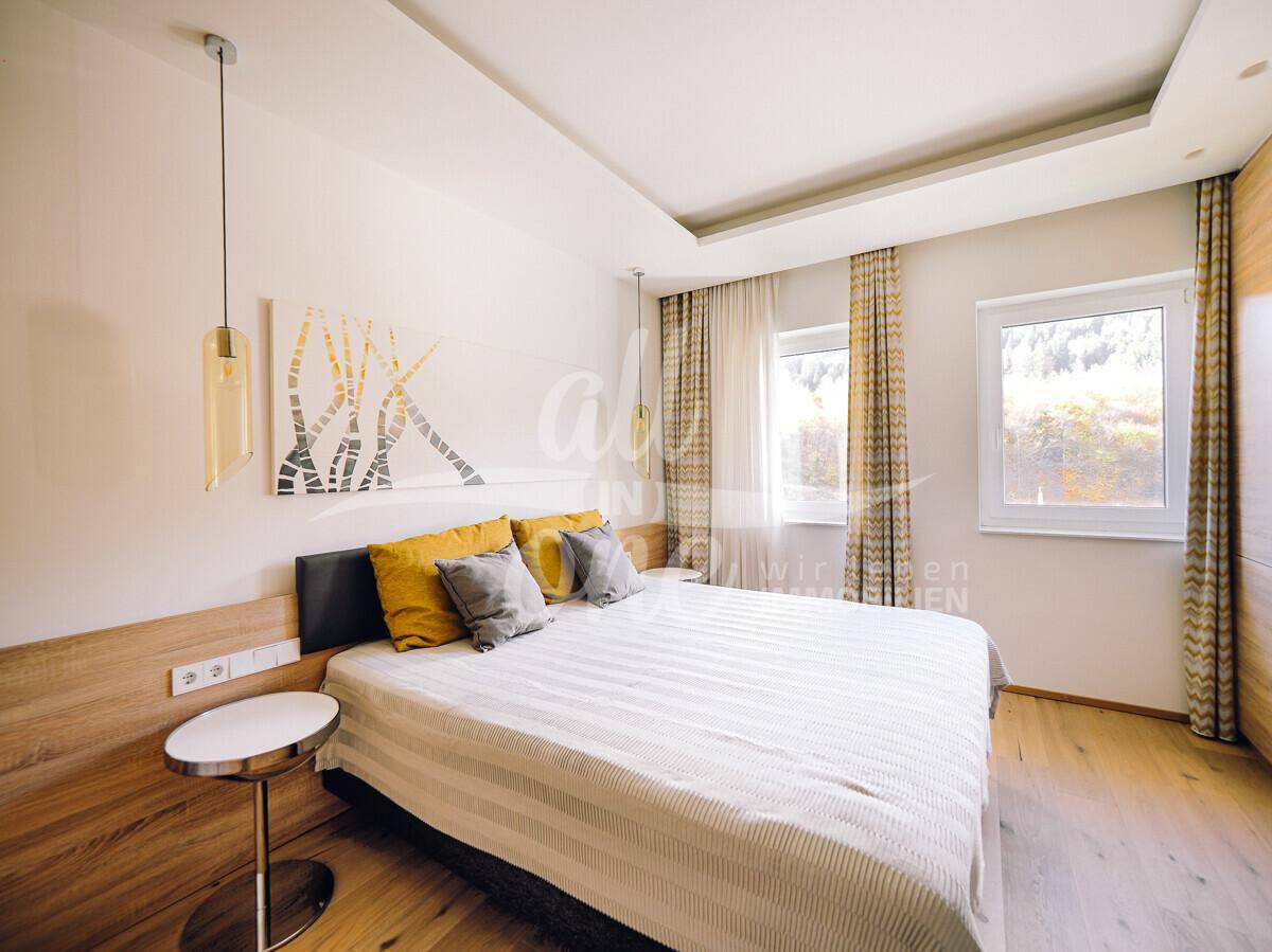 Helles Schlafzimmer mit Holzboden, großem Bett und Fenstern mit Blick ins Grüne.