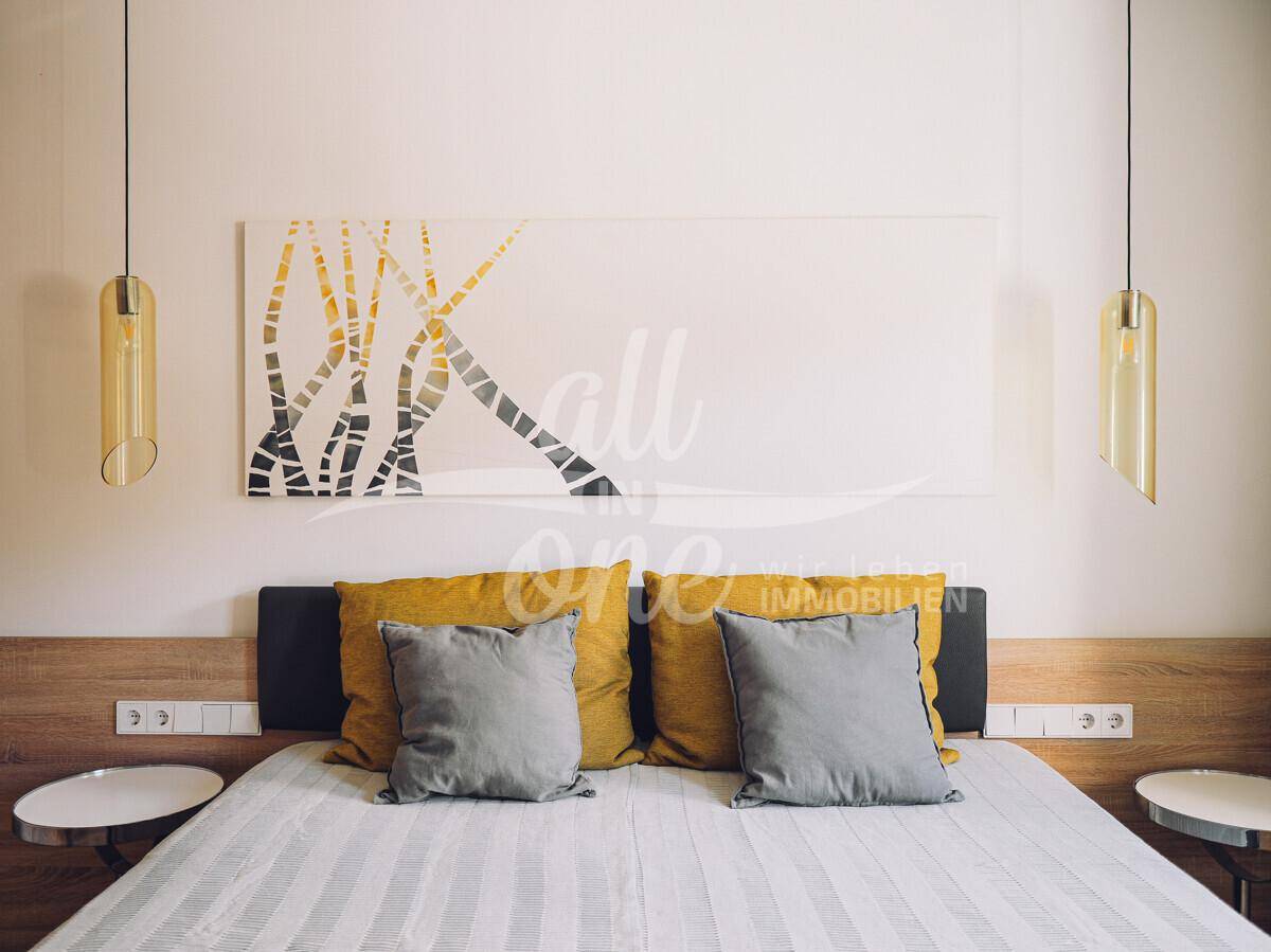 Detailansicht des Bettes im Schlafzimmer mit modernen Pendelleuchten und Kunstwerk.