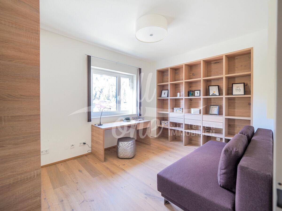 Helles Arbeitszimmer mit Holzboden, großem Bücherregal und Schreibtisch am Fenster.