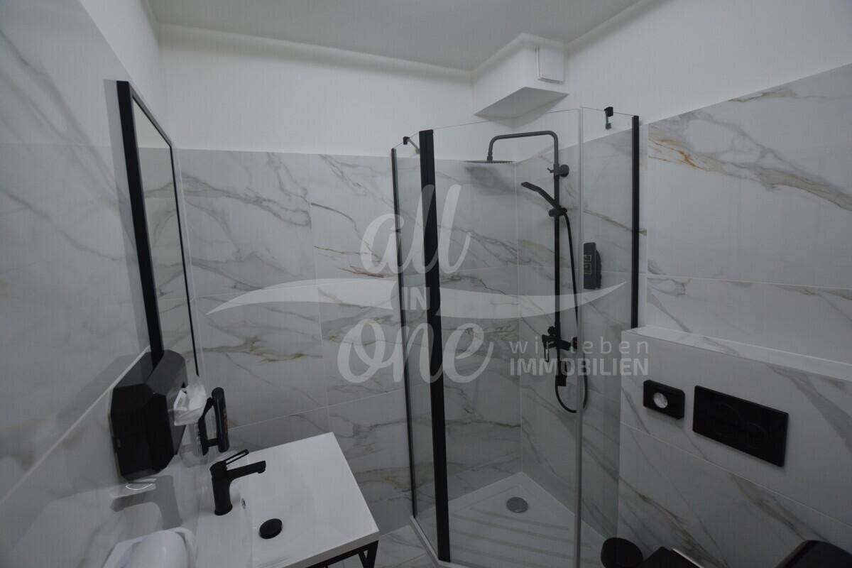 Modernes Badezimmer mit Marmoroptik-Fliesen, schwarzer Armatur und begehbarer Dusche.