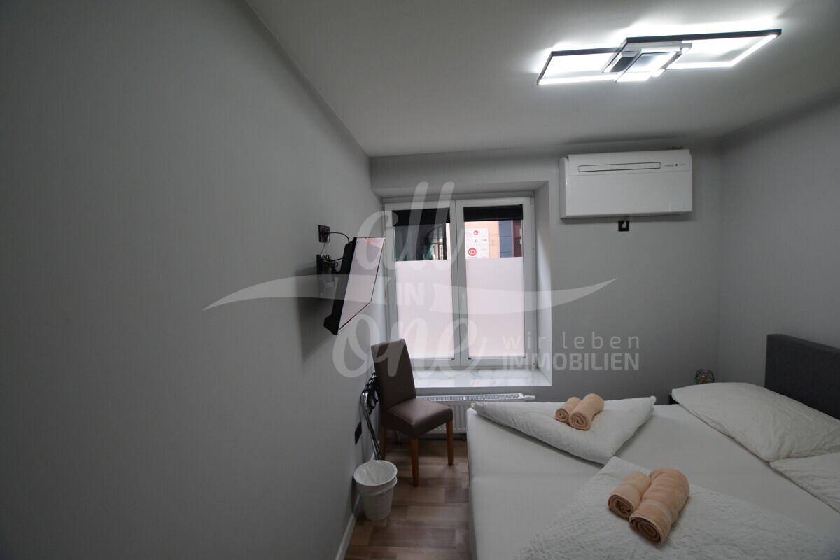 Schlafzimmer mit Doppelbett, Klimaanlage, Wandfernseher und Fenster mit Blick nach draußen.