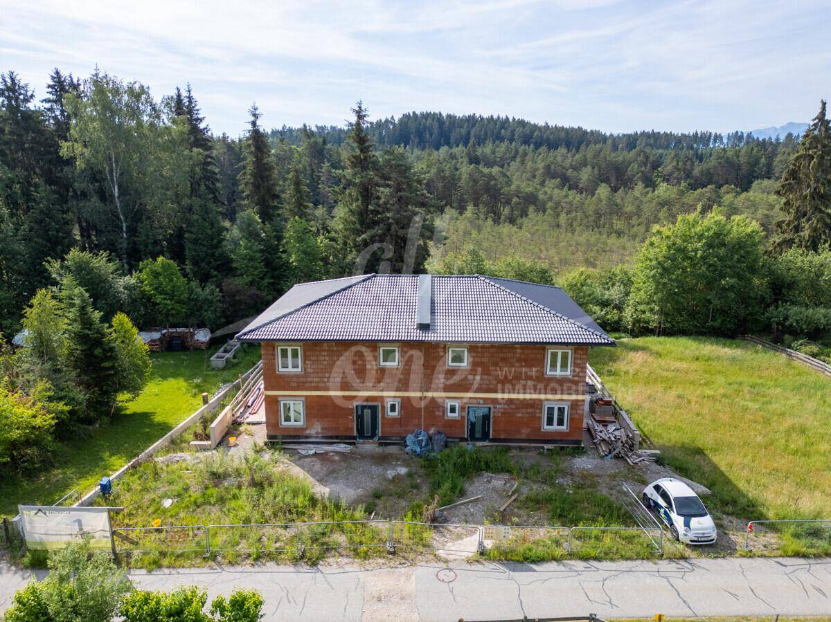 Frontansicht des Neubaus im Rohbau mit großen Fenstern und ländlicher Umgebung.