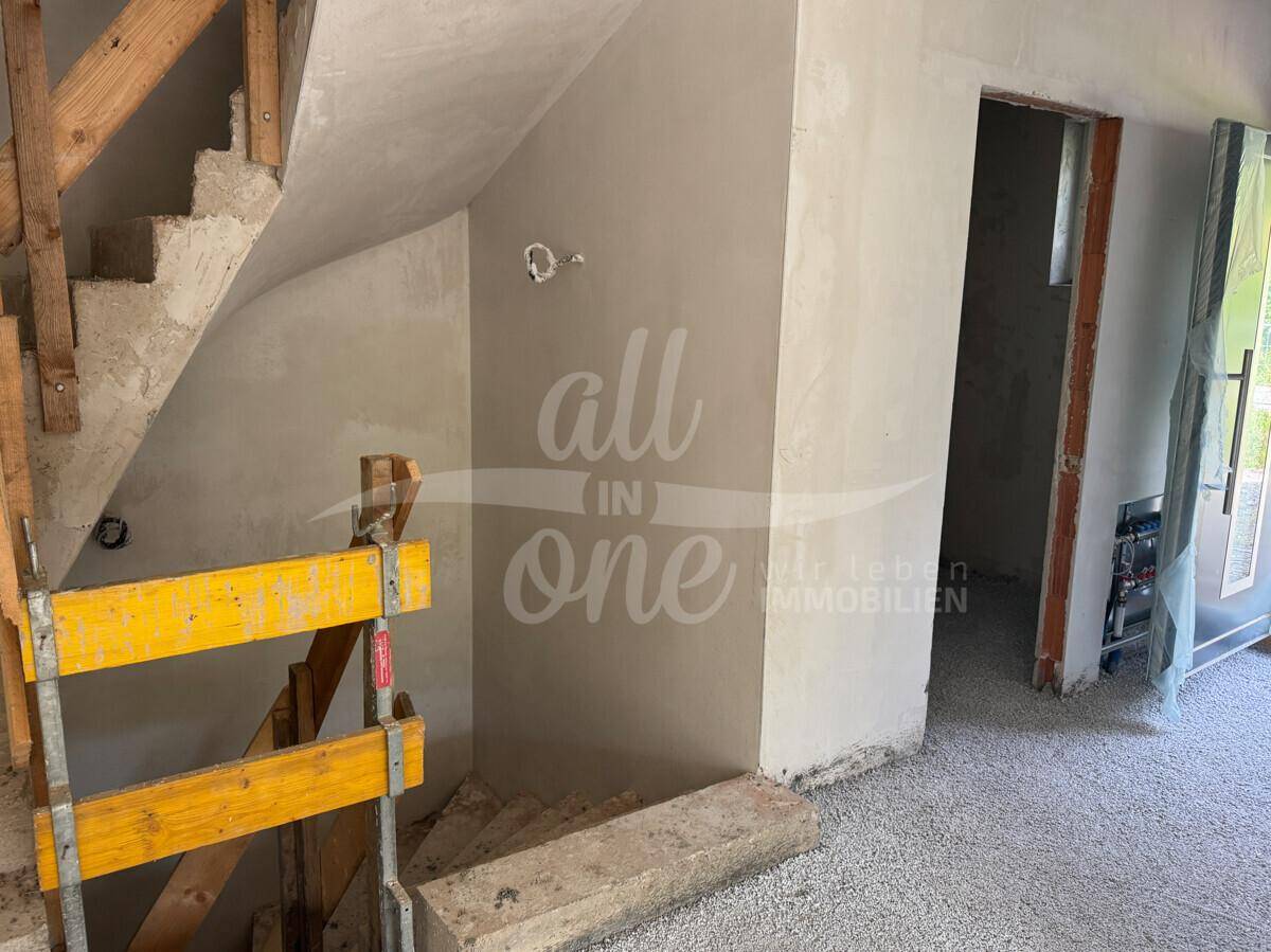 Unfertiger Treppenbereich im Rohbau mit sichtbaren Holzstufen und Putzwänden.