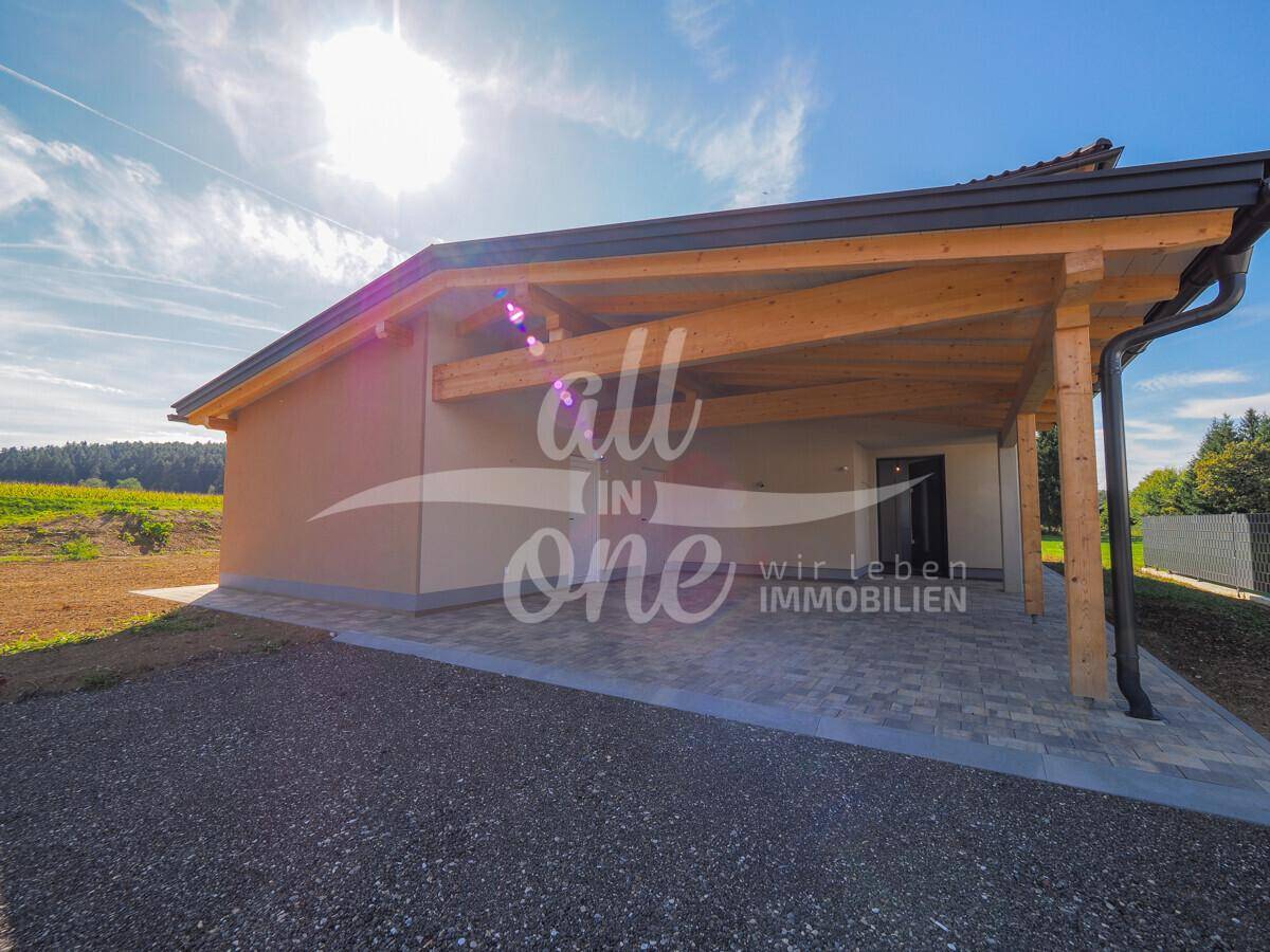 Modernes Haus mit Holz-Carport und gepflasterter Einfahrt in ländlicher Umgebung.