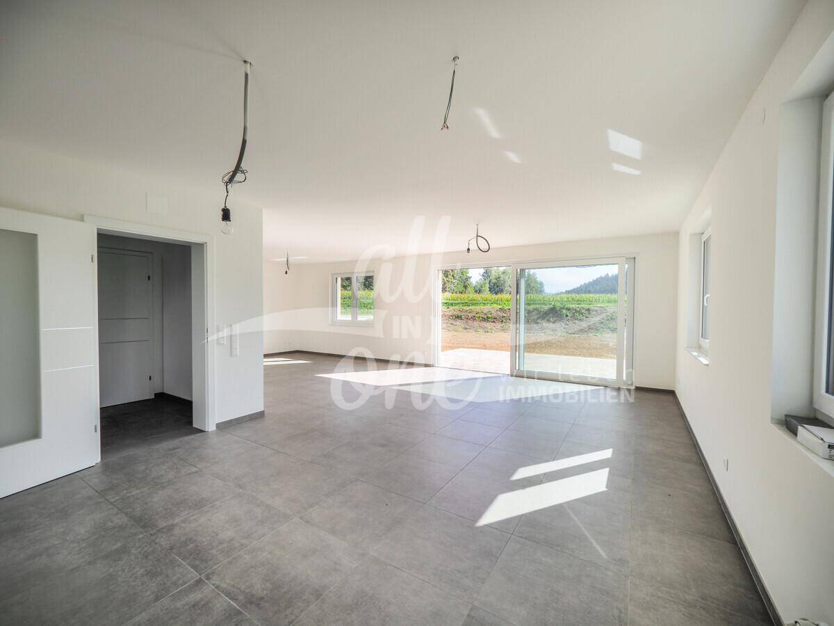 Lichtdurchflutetes Wohnzimmer mit großen Fenstern und Schiebetür zur Außenterrasse.