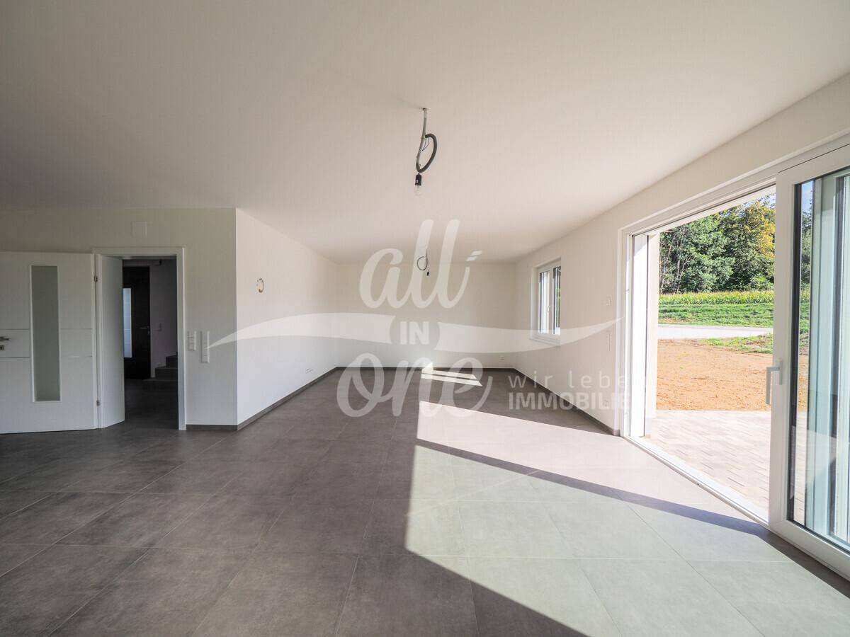 Geräumiges Wohnzimmer mit Fliesenboden und viel Tageslicht, offen zum Eingangsbereich.