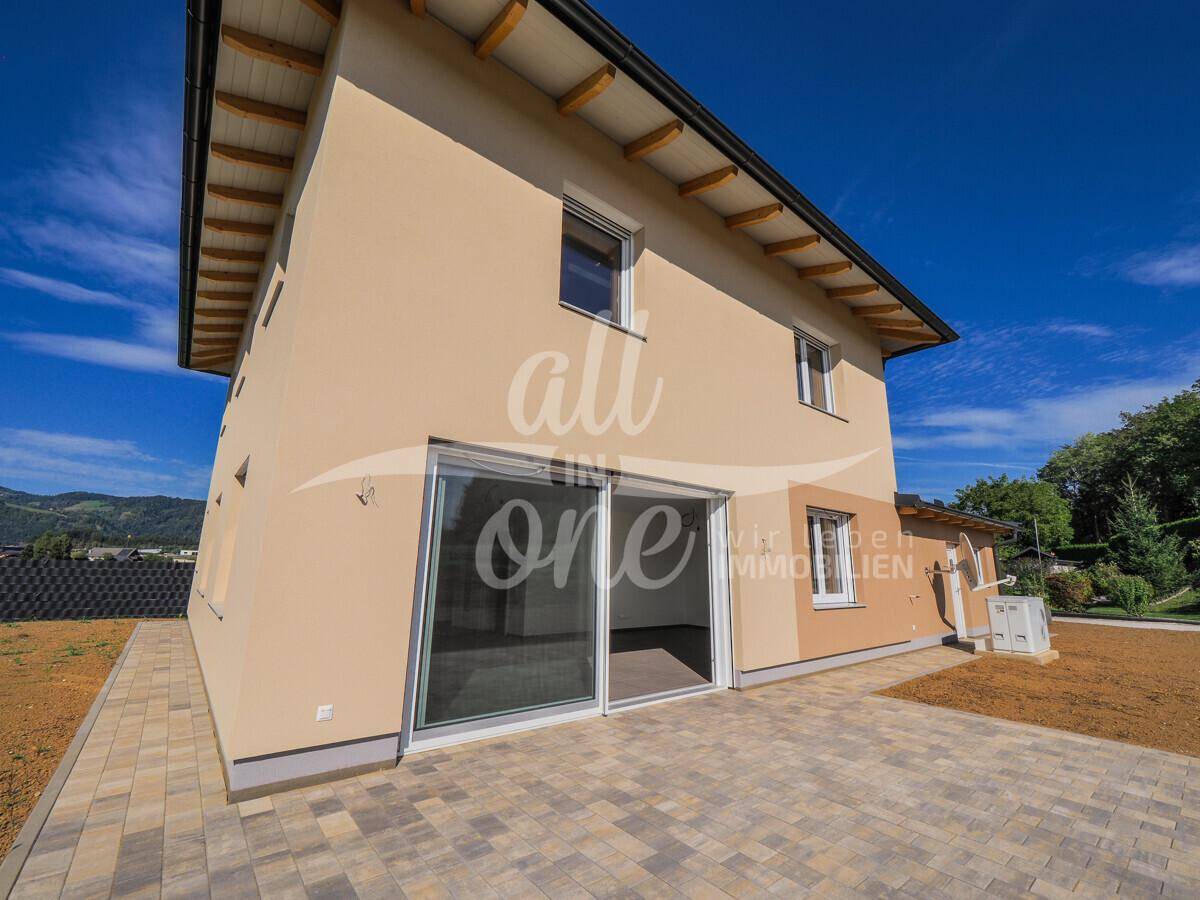 Seitenansicht des Hauses mit großer Terrasse und Schiebetüren zum hellen Innenbereich.