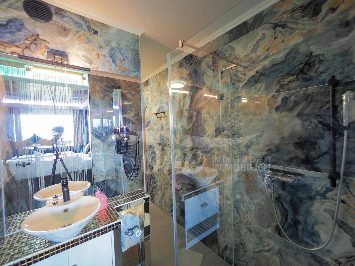 Luxuriöses Badezimmer mit zwei Waschbecken, großer begehbarer Dusche und auffälligen Marmorfliesen.