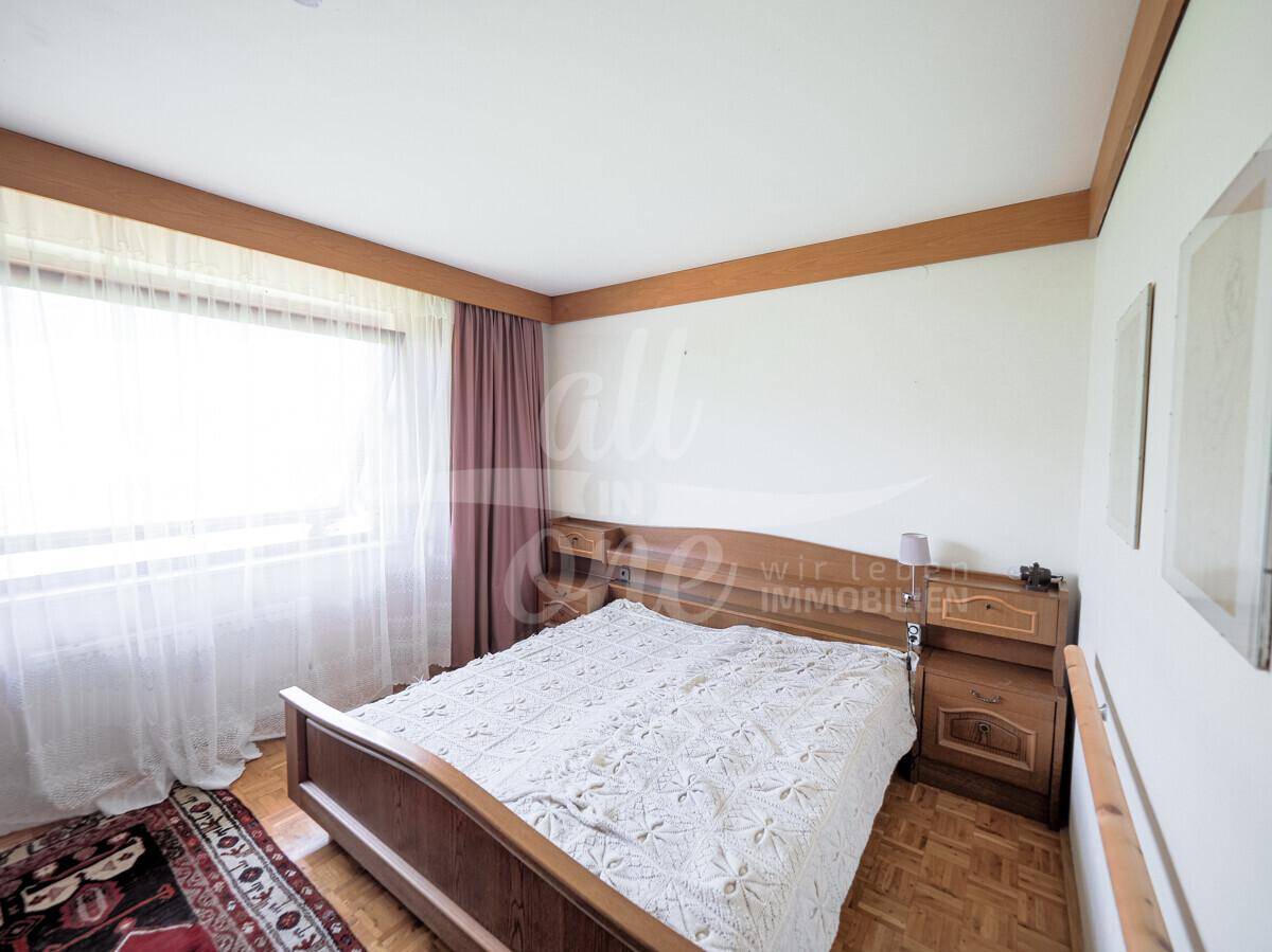 Helles Schlafzimmer mit Holzbett, Parkettboden und großem Fenster mit Vorhängen.