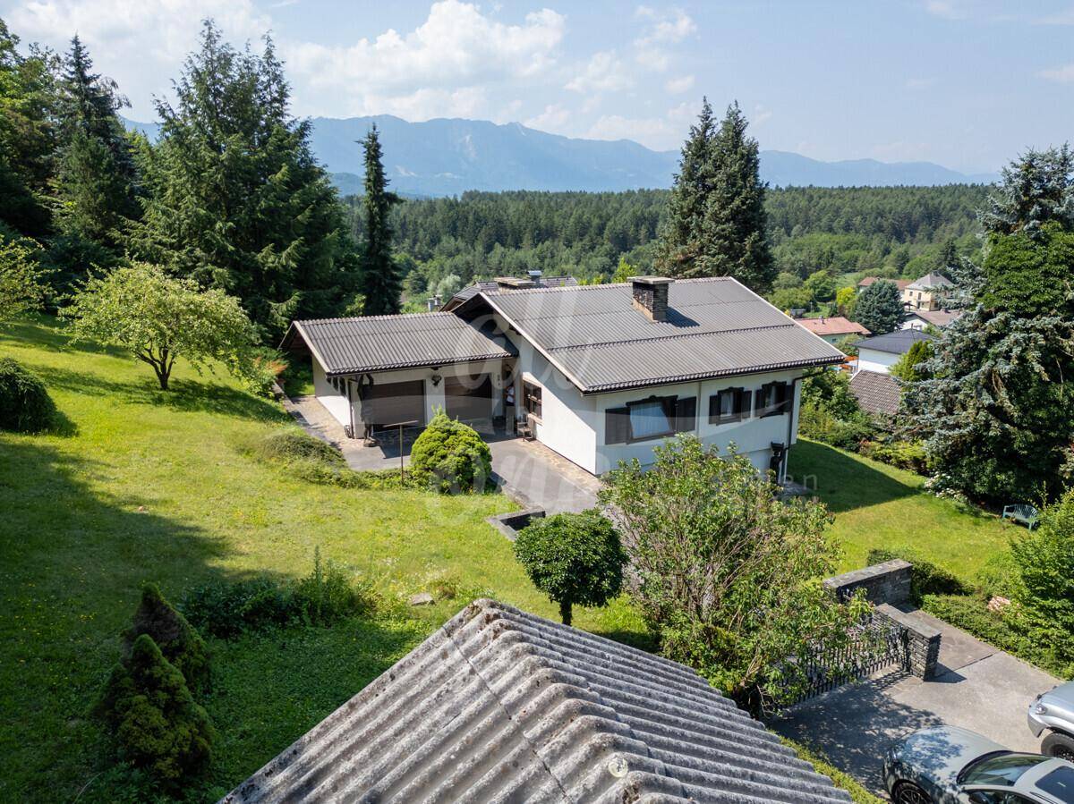 Panoramablick auf das Haus und die weite Landschaft mit Bergen im Hintergrund und viel Grün.