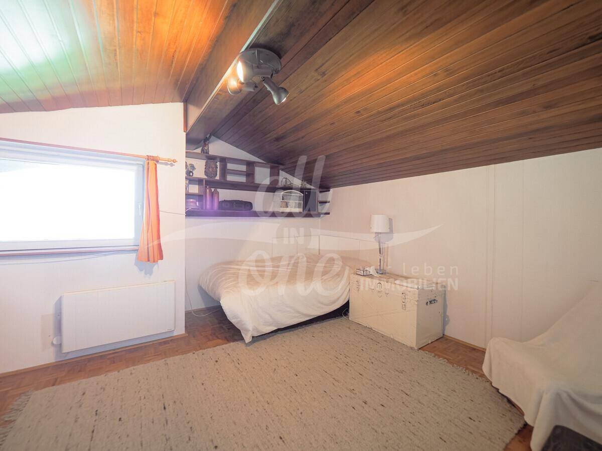Helles Schlafzimmer im Dachgeschoss mit schräger Holzdecke und Fenster.