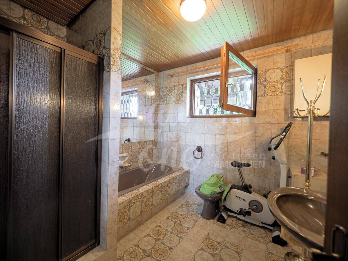 Gefliestes Badezimmer im 80er-Jahre-Stil mit Badewanne, Dusche und Fenster.