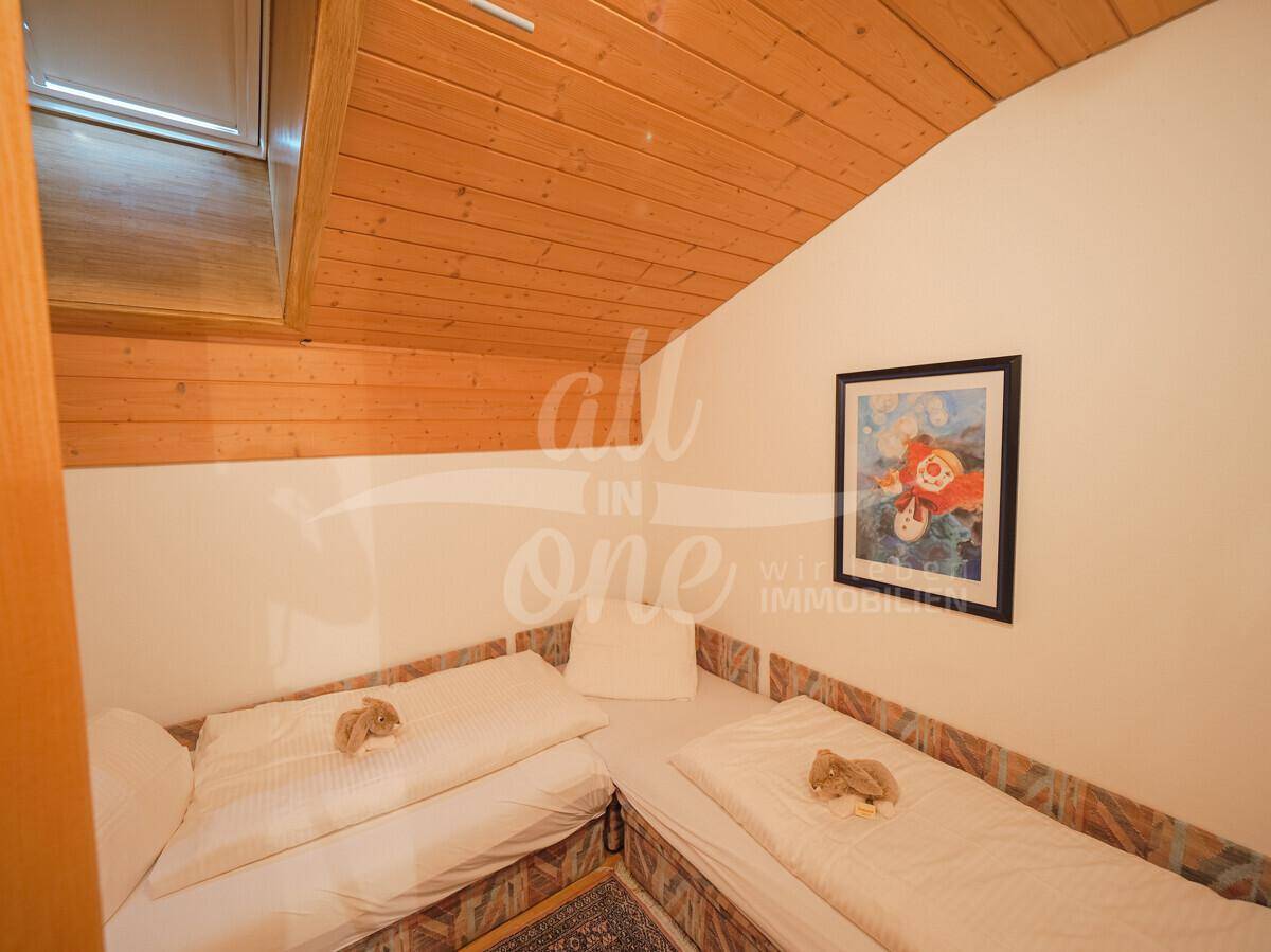 Kleines Schlafzimmer mit zwei Einzelbetten, Holzbalkendecke und schräger Dachschräge.