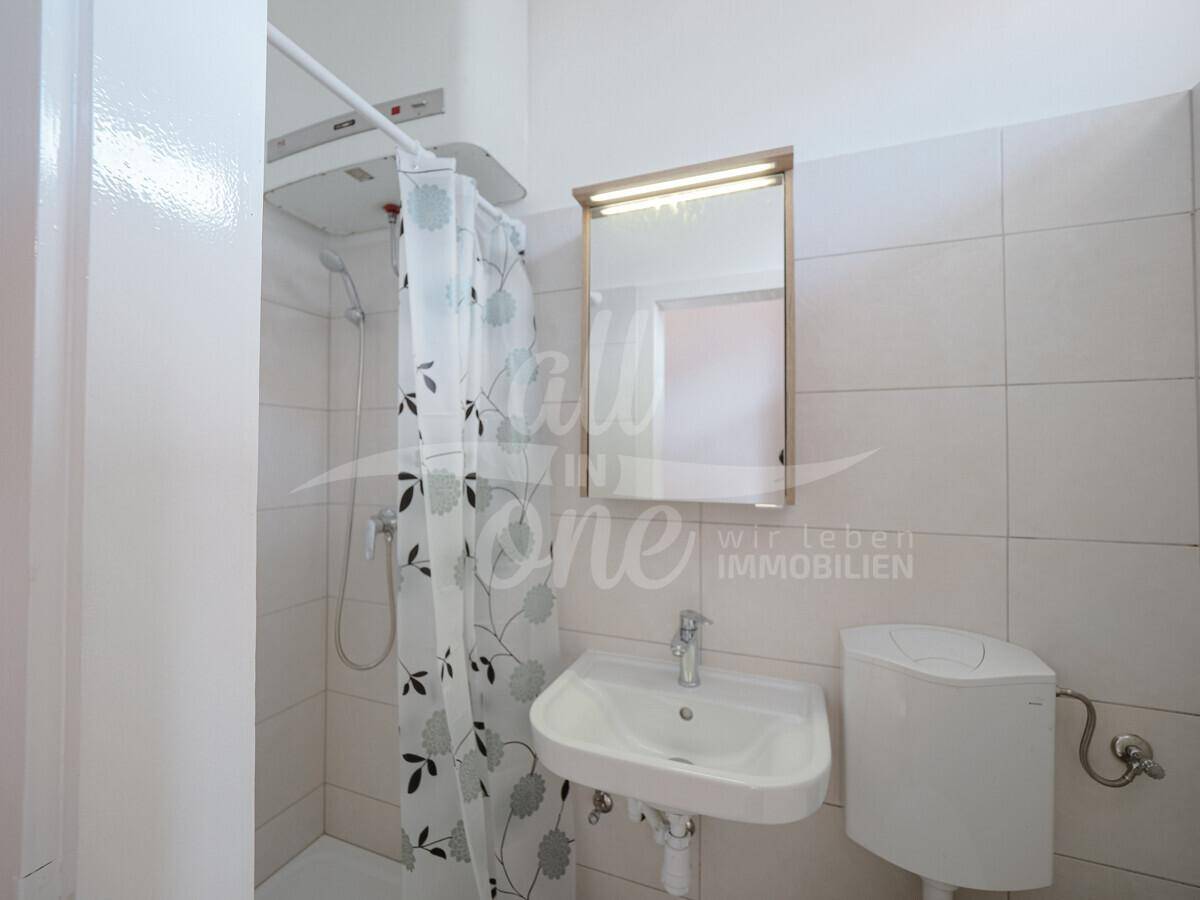 Kleines Badezimmer mit Duschbereich und WC, hell gefliest und funktional eingerichtet.