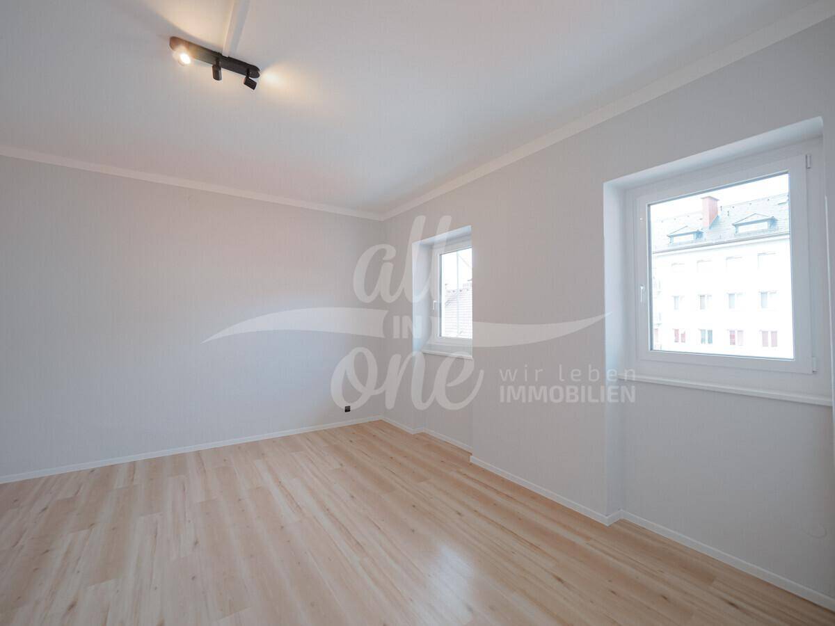 Helles Zimmer mit zwei Fenstern und hellem Laminatboden, bietet viel Tageslicht.