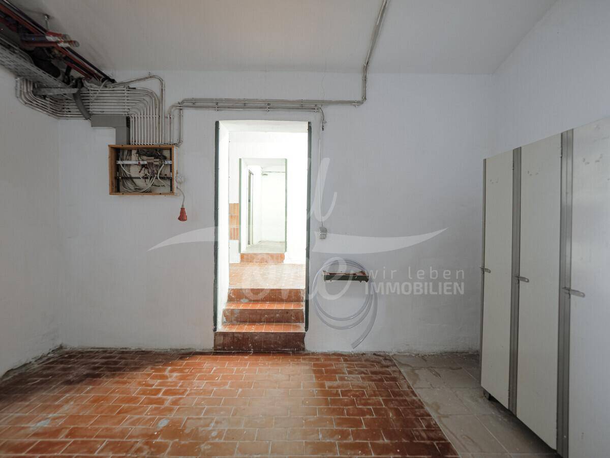 Kellerraum mit Zugang zu weiteren Bereichen, ausgestattet mit Ziegelboden und Schränken.