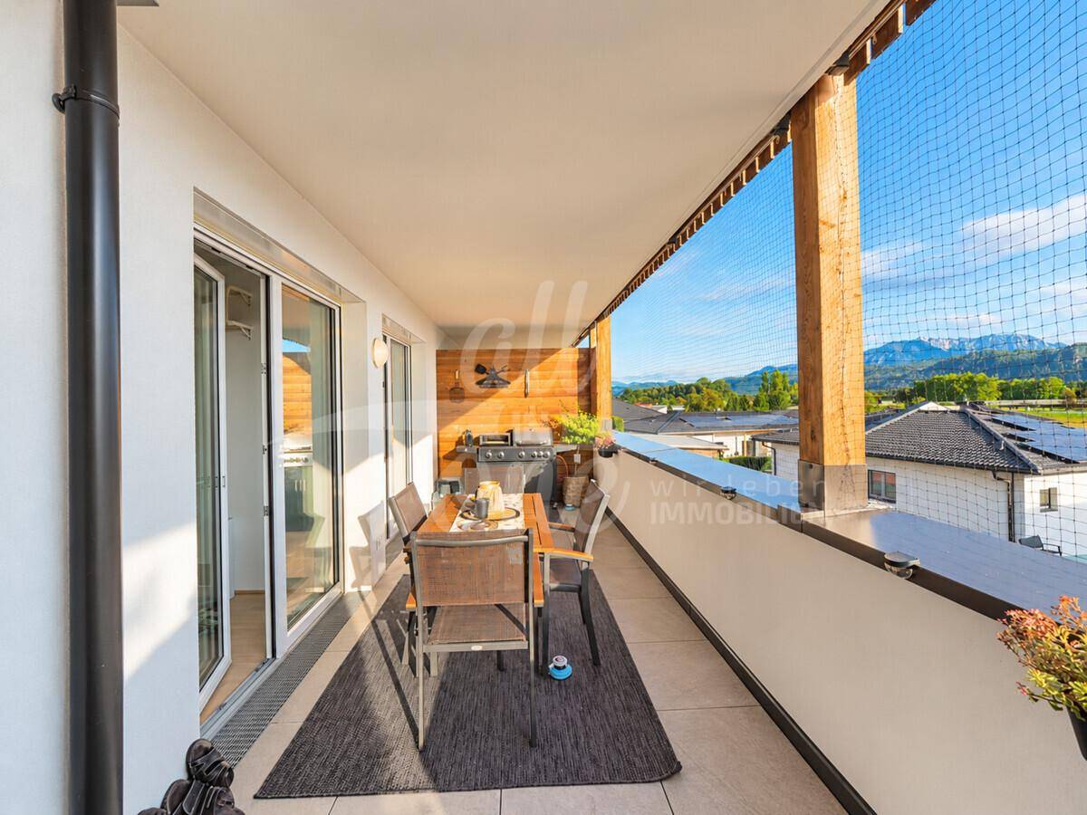 Heller Balkon mit Grillbereich, Esstisch und Zugang zum Innenraum, umgeben von Natur.