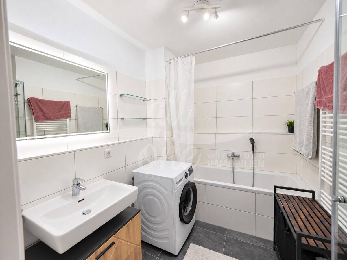 Modernes Badezimmer mit Badewanne, Waschbecken, Spiegel und integrierter Waschmaschine.