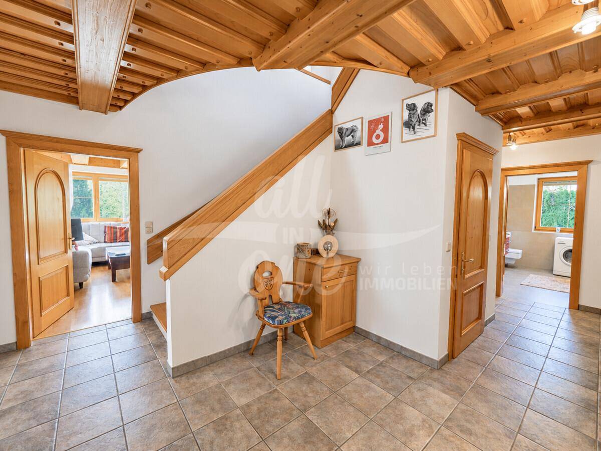 Heller Eingangsbereich mit Holztreppe, Fliesenboden und Zugang zu weiteren Räumen.