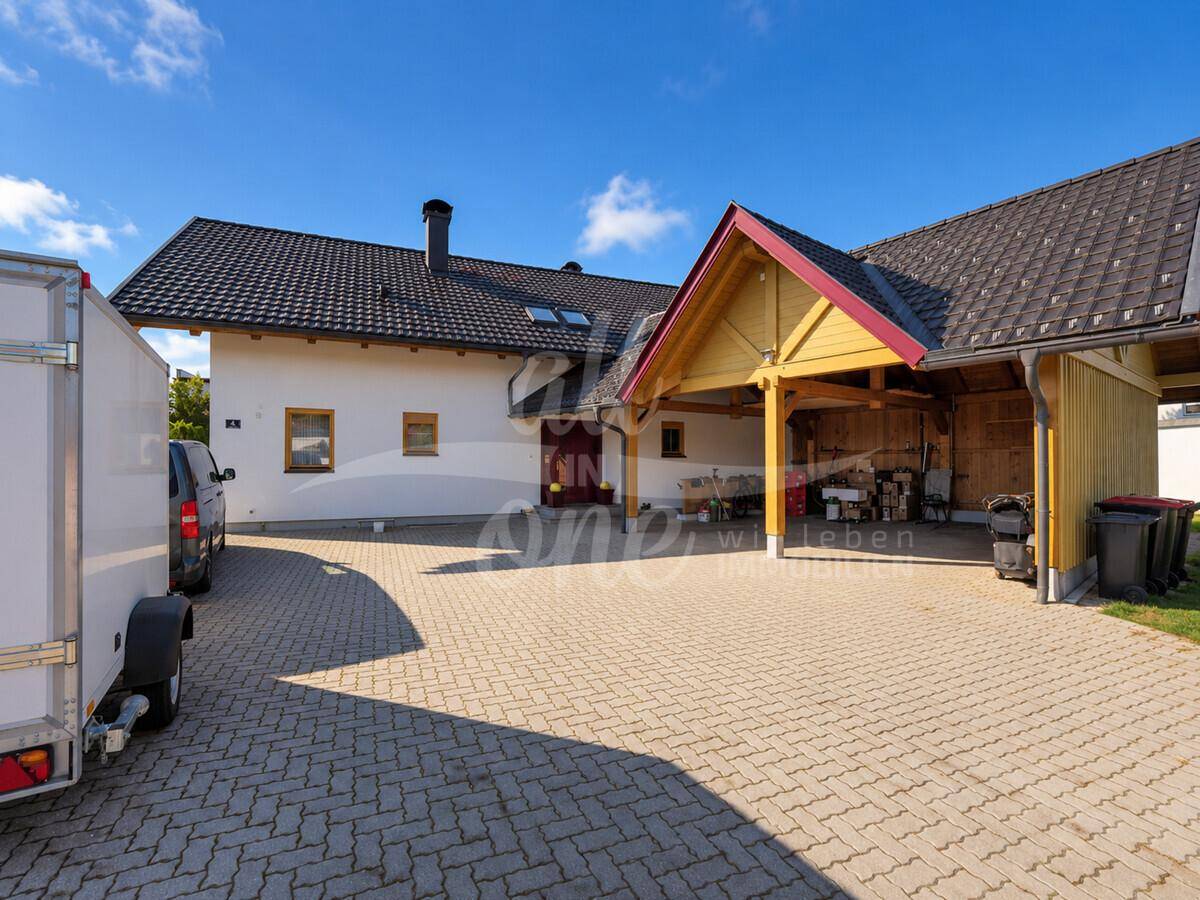 Zufahrt zum Haus mit gepflastertem Bereich und einem überdachten Carport.