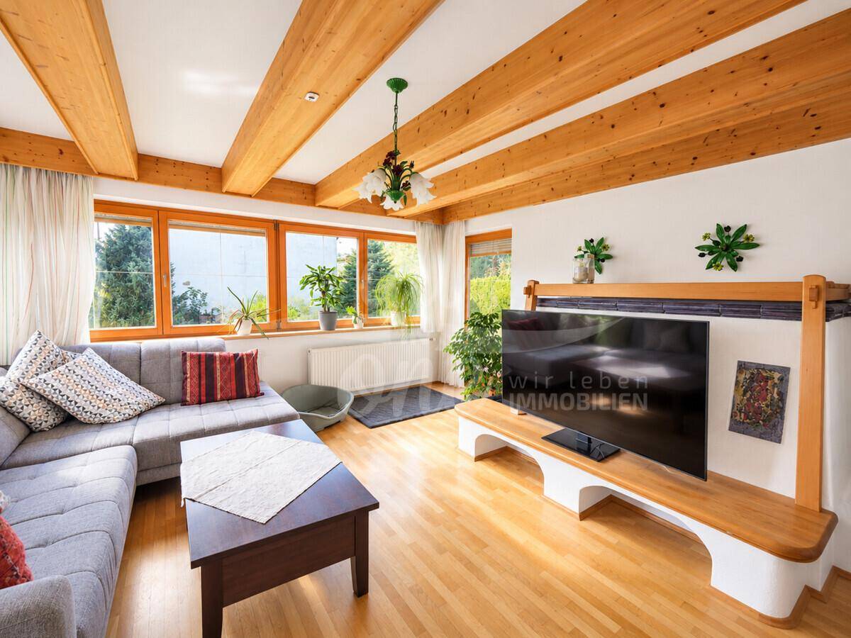 Gemütliches Wohnzimmer mit Holzbalkendecke, großem Sofa und Blick ins Grüne.