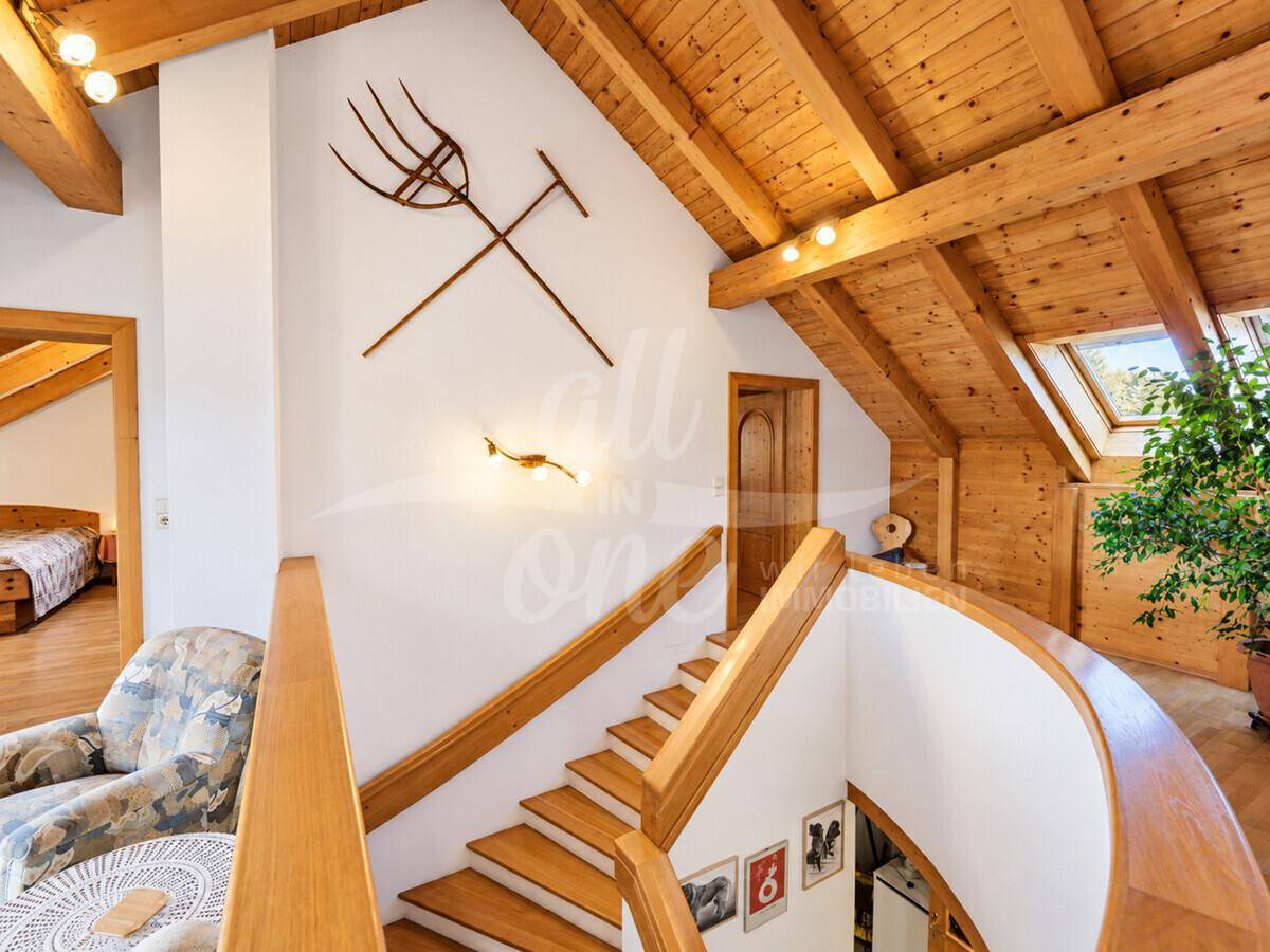 Offenes Treppenhaus mit Holzgeländer und sichtbaren Holzbalken, das die oberen Etagen verbindet.