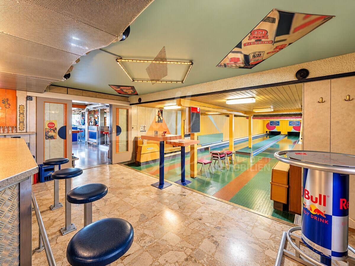 Innenansicht einer Kegelbahn mit Barbereich, Sitzgelegenheiten und Blick auf die Bowlingbahnen.