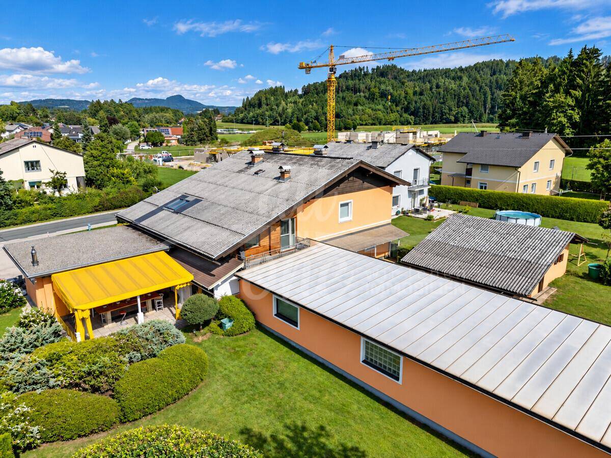 Luftaufnahme des Gebäudes mit angrenzendem Garten, einem Kran im Hintergrund und umliegender Bebauung.