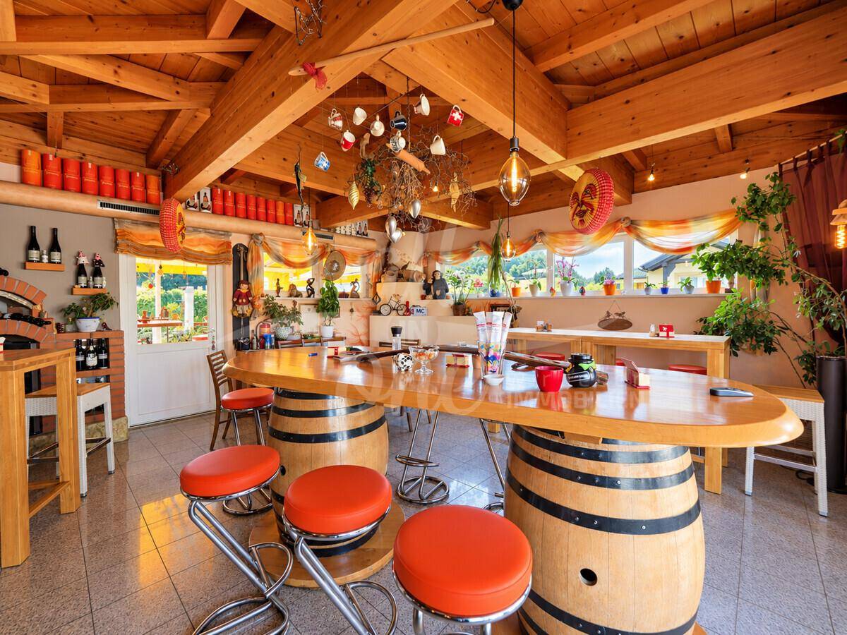 Rustikaler Restaurantbereich mit Holzbalkendecke, Fass-Tischen und orangefarbenen Hockern in gemütlicher Atmosphäre.