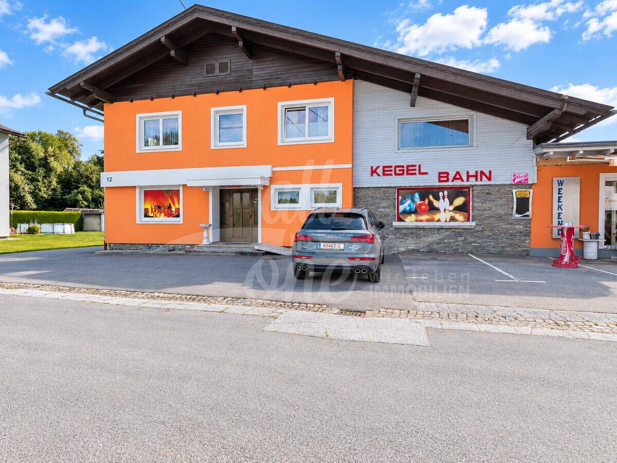 Nahaufnahme des Gebäudes mit orangefarbener Fassade, Parkplatz und Beschilderung für die Kegelbahn.