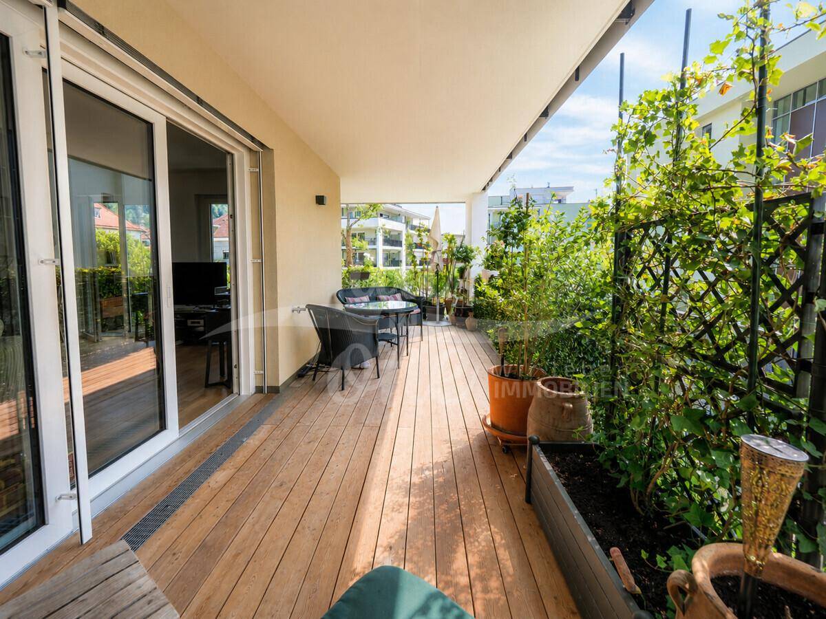 Großer Balkon mit Holzdeck, üppiger Bepflanzung und bequemen Outdoor-Möbeln für entspannte Stunden.