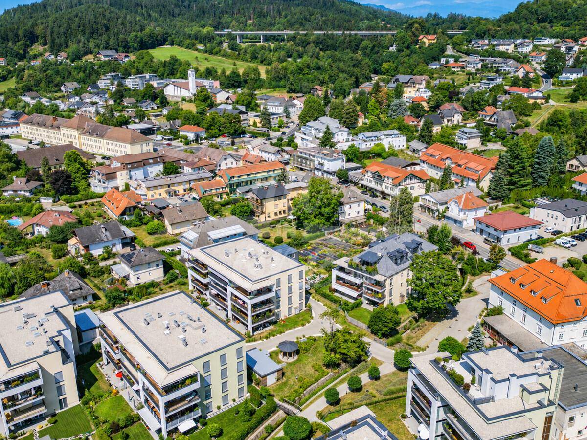 Luftaufnahme der Wohngegend mit modernen Gebäuden, viel Grün und Bergen im Hintergrund.