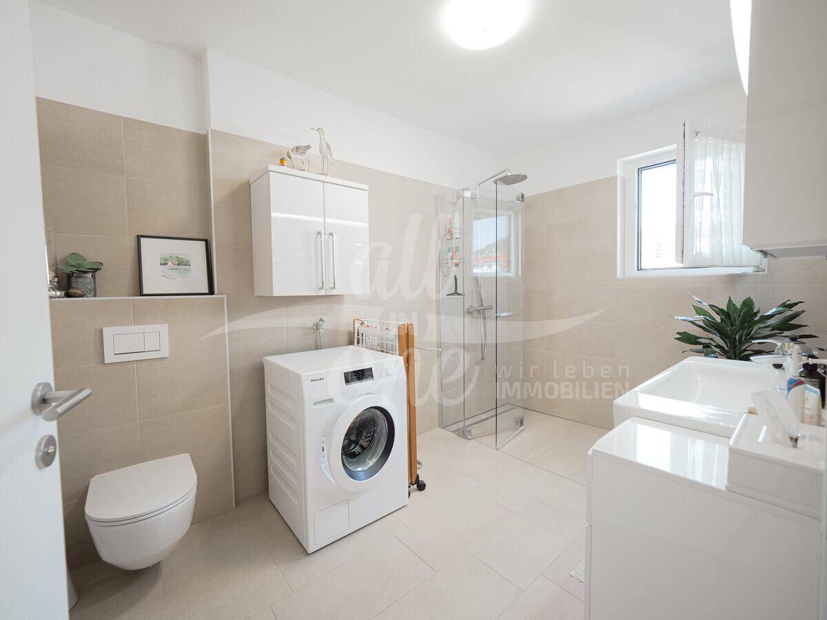 Modernes Badezimmer mit ebenerdiger Dusche, WC, Waschbecken und integrierter Waschmaschine.