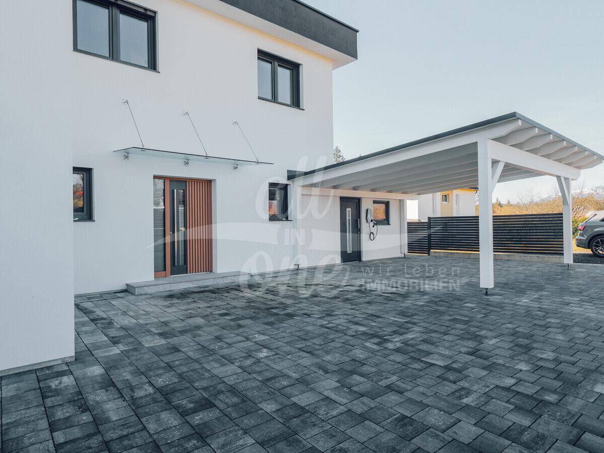 Eingangsbereich des modernen Hauses mit Carport und gepflasterter Auffahrt, bietet geschützten Zugang.