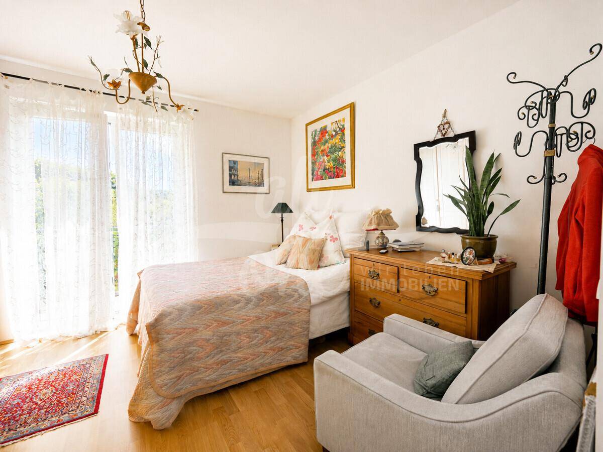 Helles Schlafzimmer mit Einzelbett, Holzkommode und großen Fenstern für viel Tageslicht.