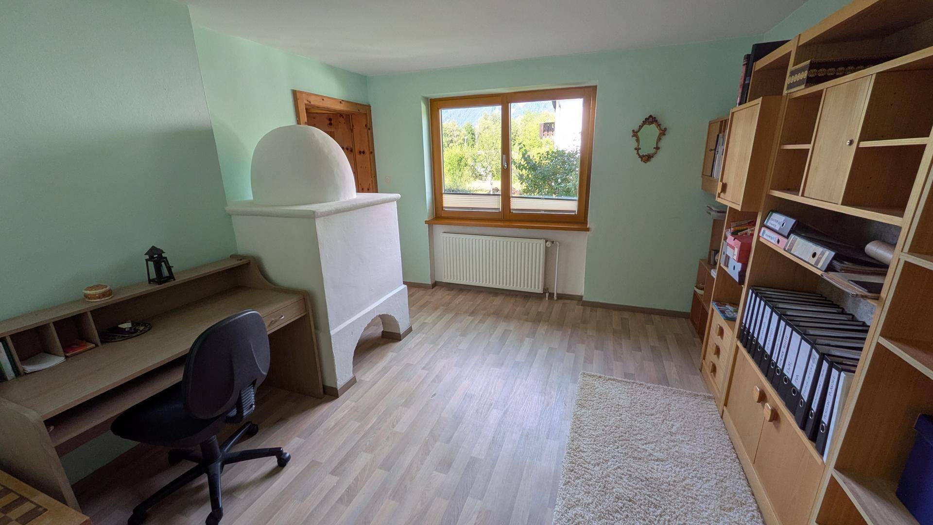 Helles Arbeitszimmer mit traditionellem Kachelofen und Blick ins Grüne.