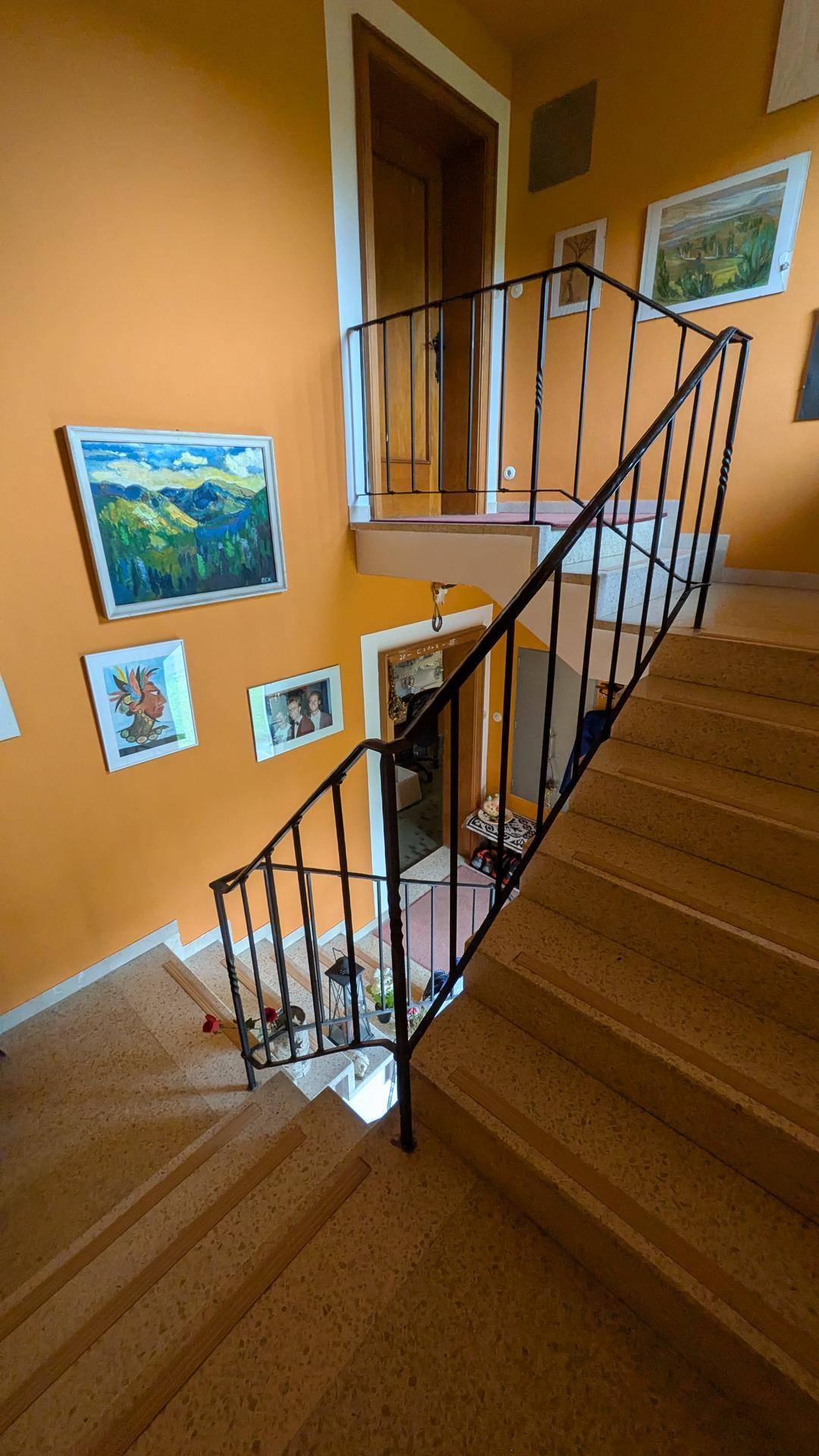 Treppenhaus mit orangefarbenen Wänden und Bildern von Berglandschaften.