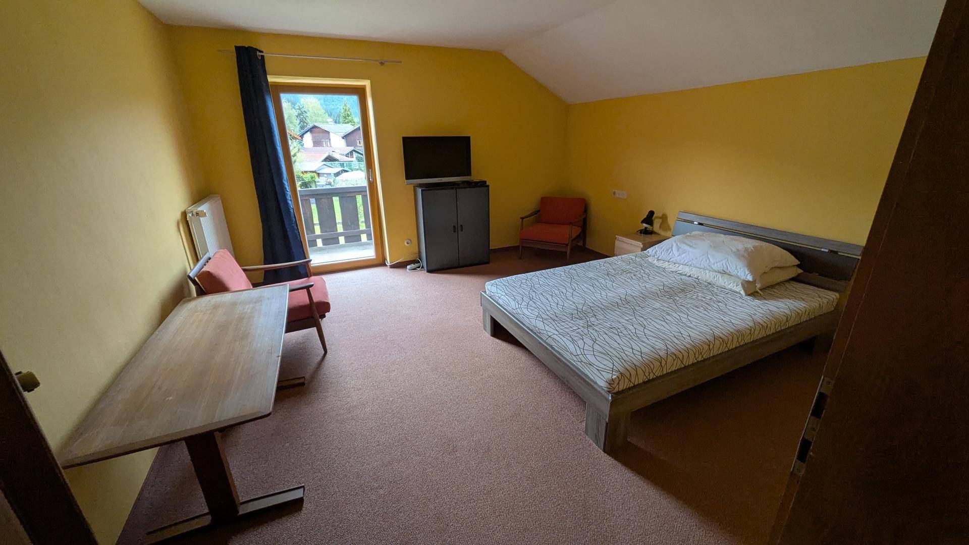 Geräumiges Schlafzimmer mit Doppelbett, gelben Wänden und Zugang zum Balkon.