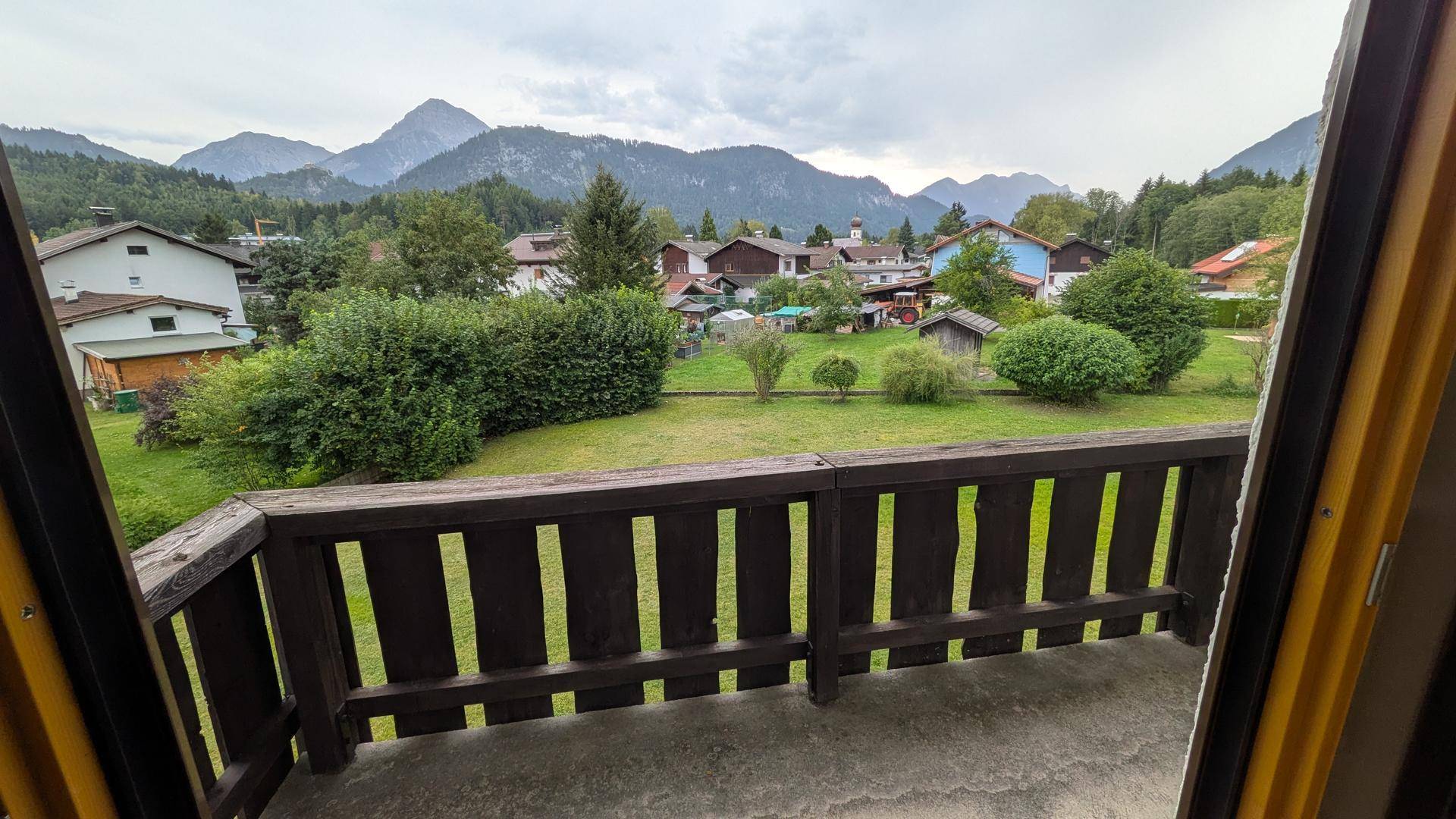 Balkon mit Holzgeländer und weitem Blick über das Dorf und die Berglandschaft.