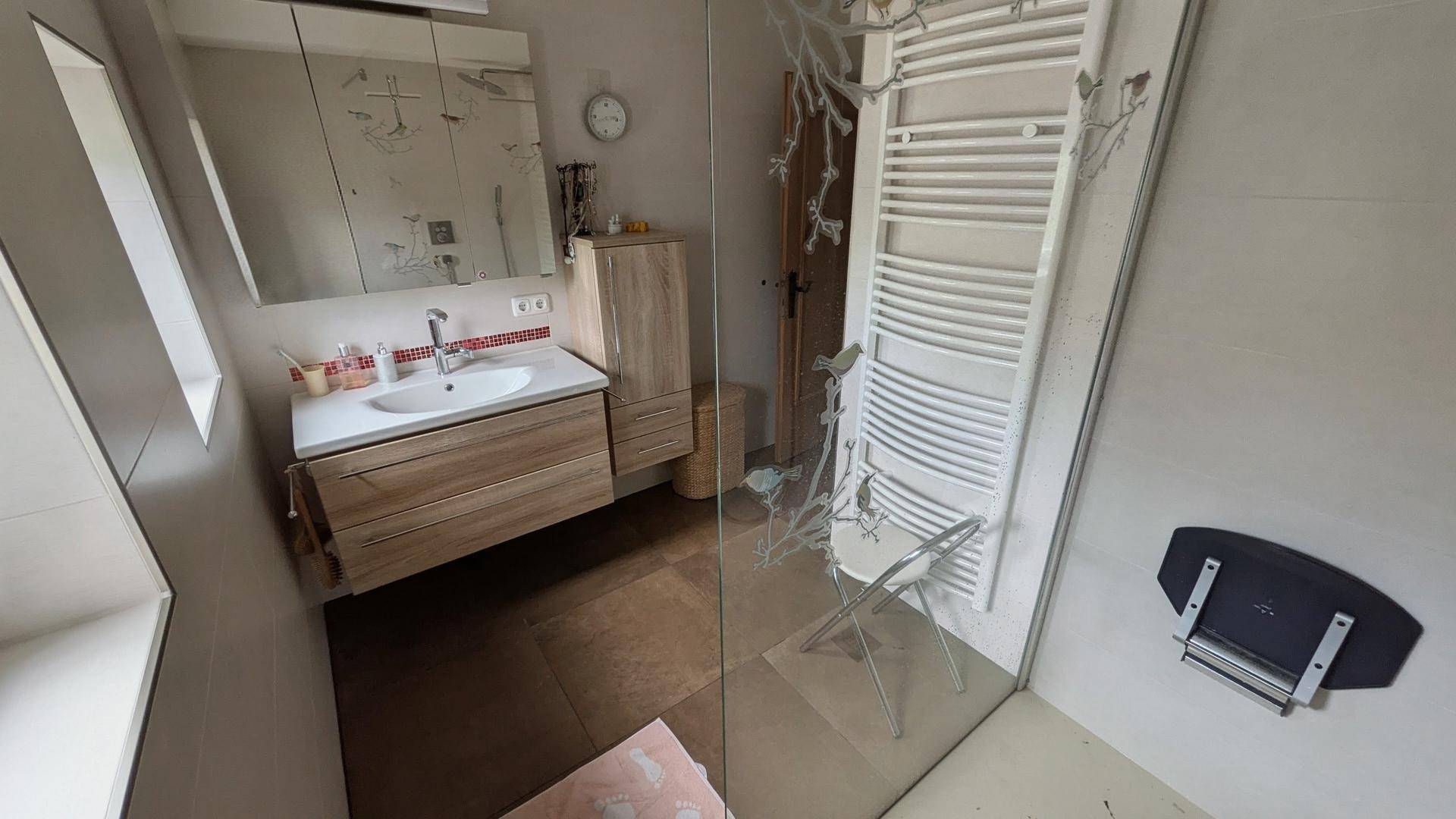 Modernes Badezimmer mit Dusche, Einzelwaschbecken und beheiztem Handtuchhalter unter Dachschräge.