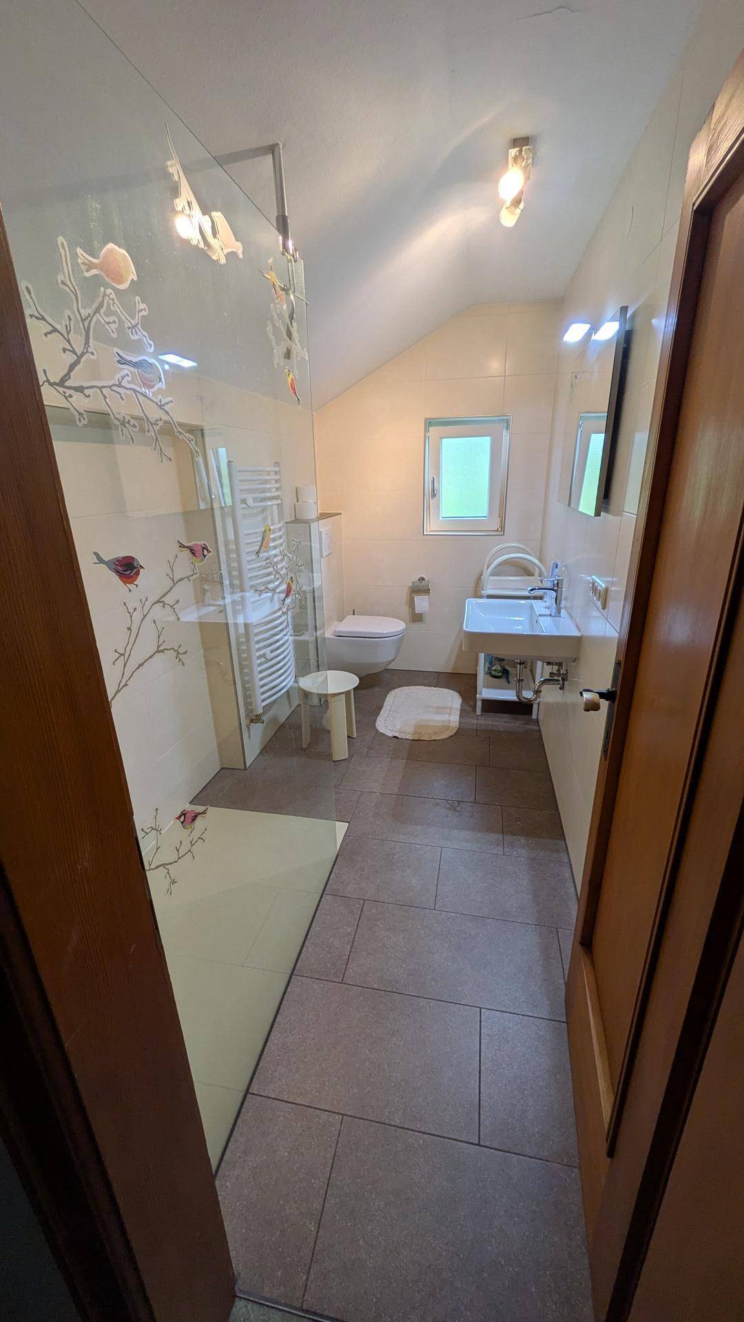 Helles Badezimmer mit Dusche, WC, Waschbecken und Fenster unter der Dachschräge.