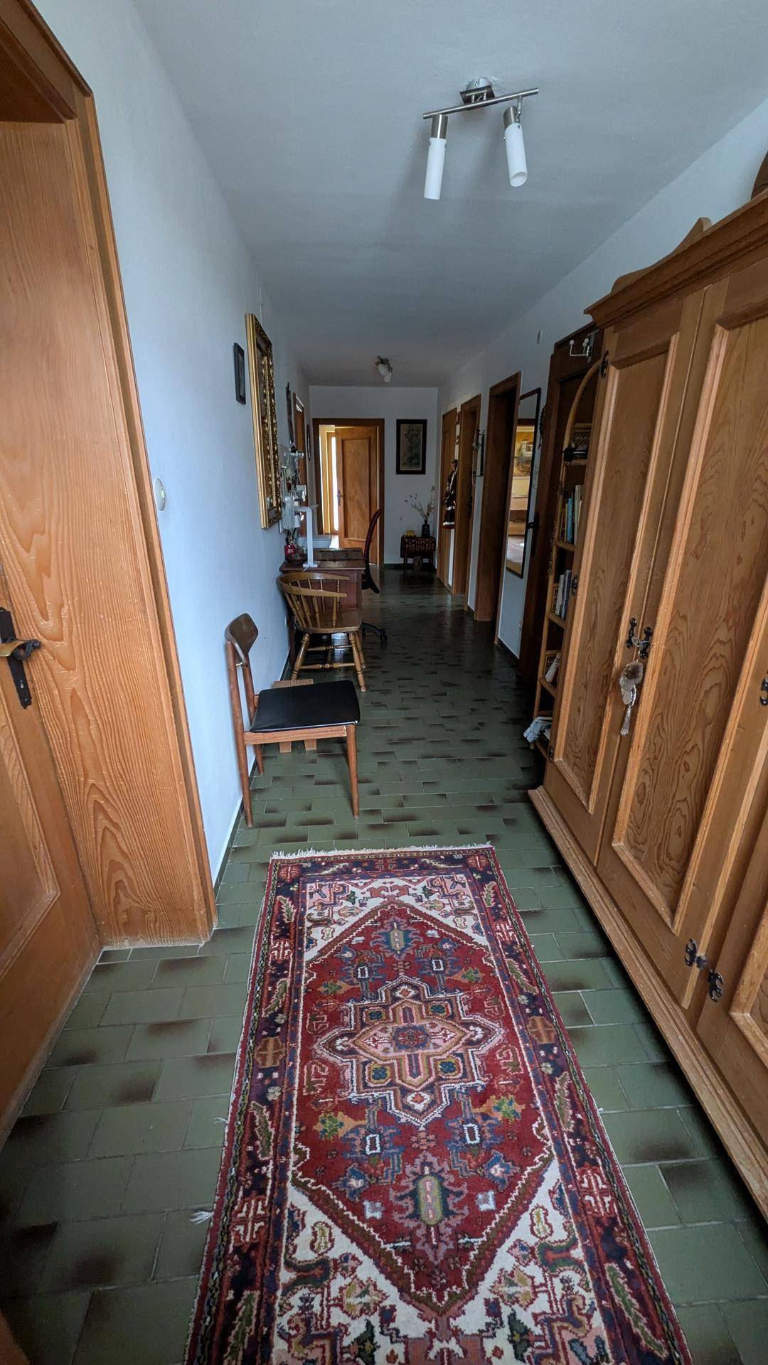 Langer Flur mit gemustertem Teppich, Holzmöbeln und Fliesenboden.