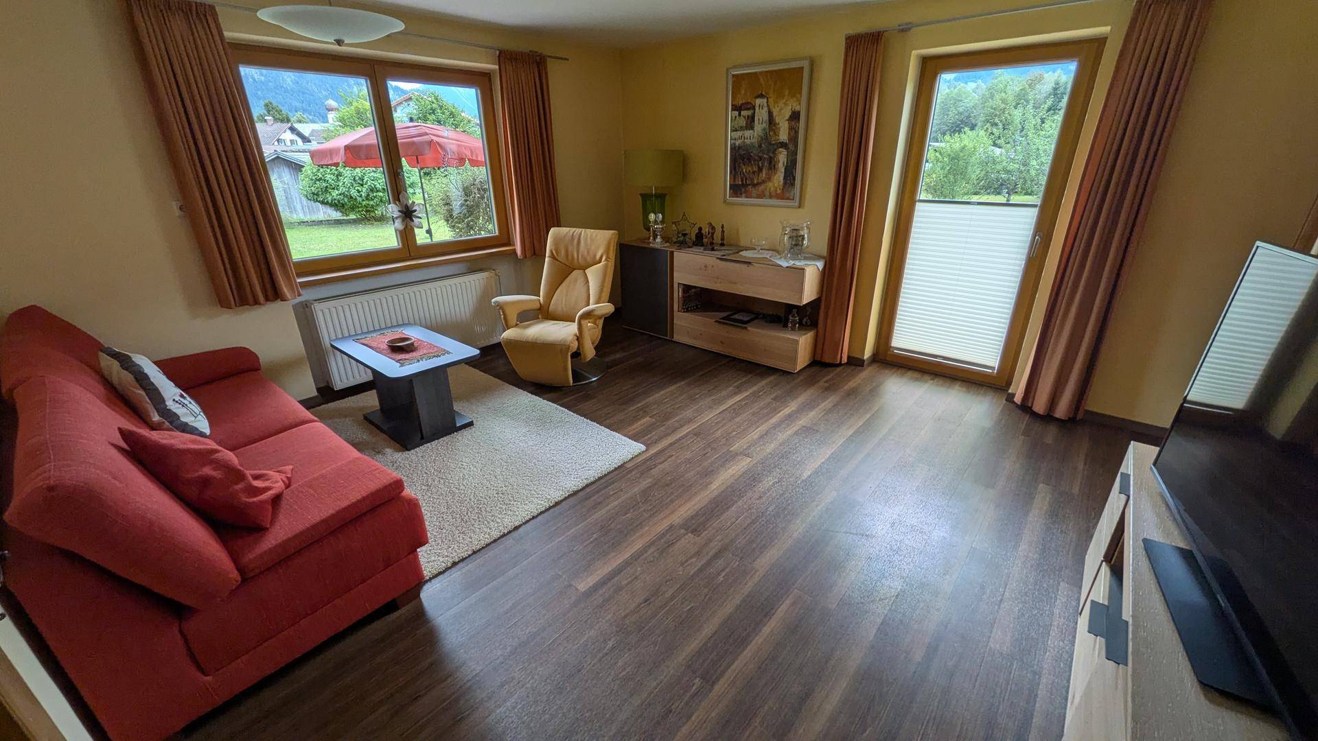 Gemütliches Wohnzimmer mit rotem Sofa, dunklem Laminatboden und Zugang zum Garten.