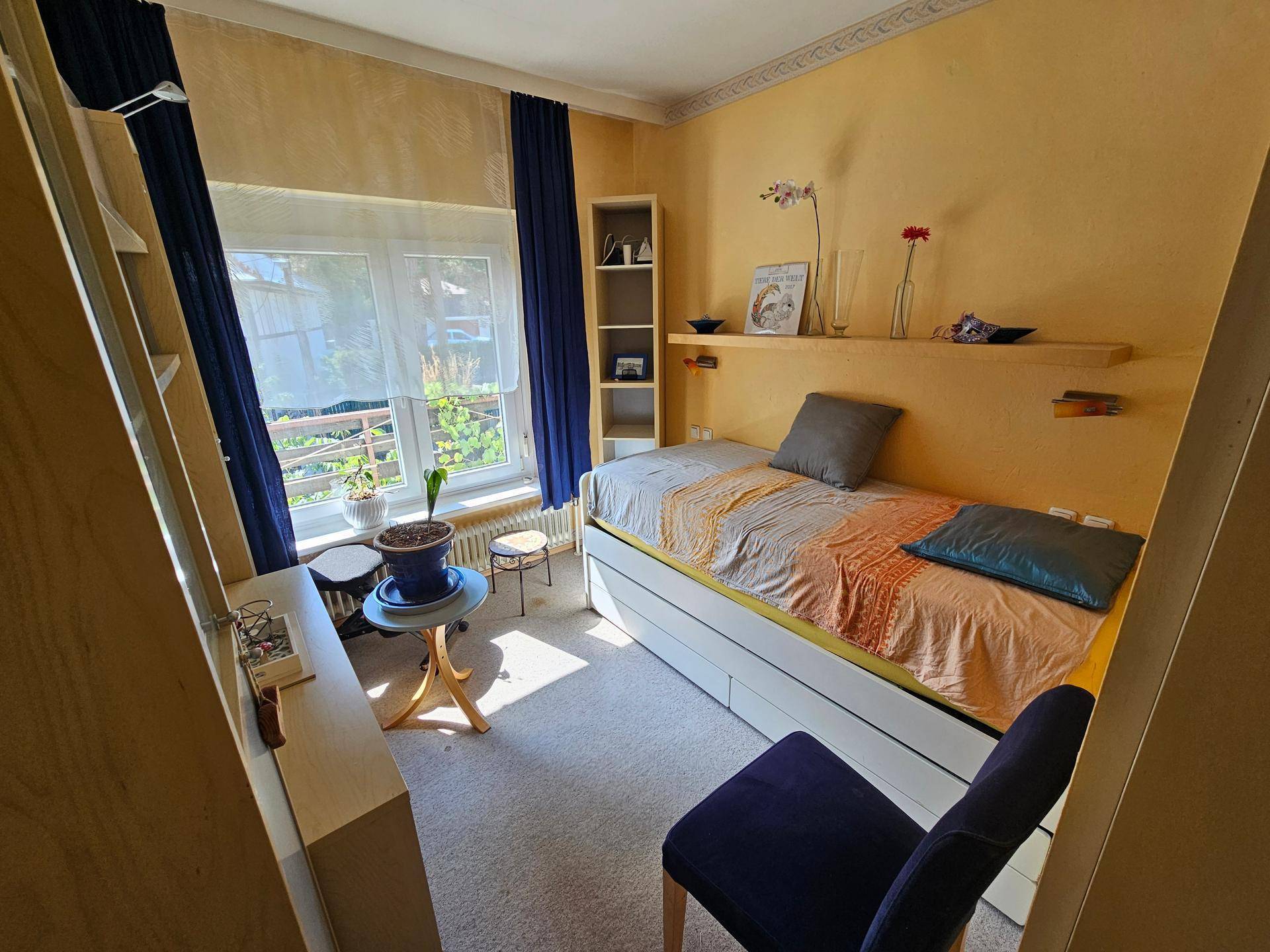 Schlafzimmer mit Einzelbett, Teppichboden und einem Fenster mit Blick ins Grüne.