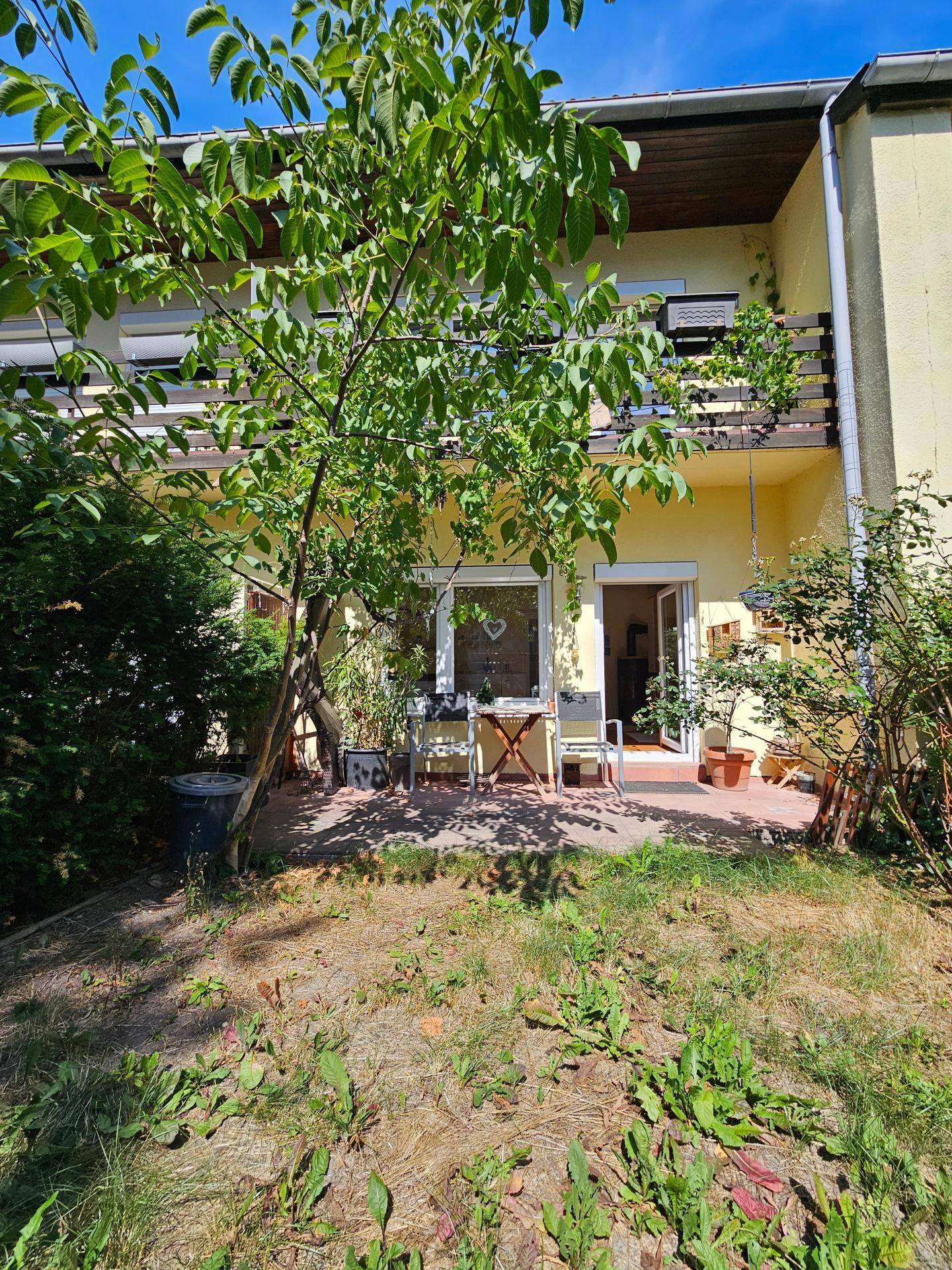 Hinterhofgarten mit kleiner gepflasterter Terrasse und einem schattenspendenden Baum.