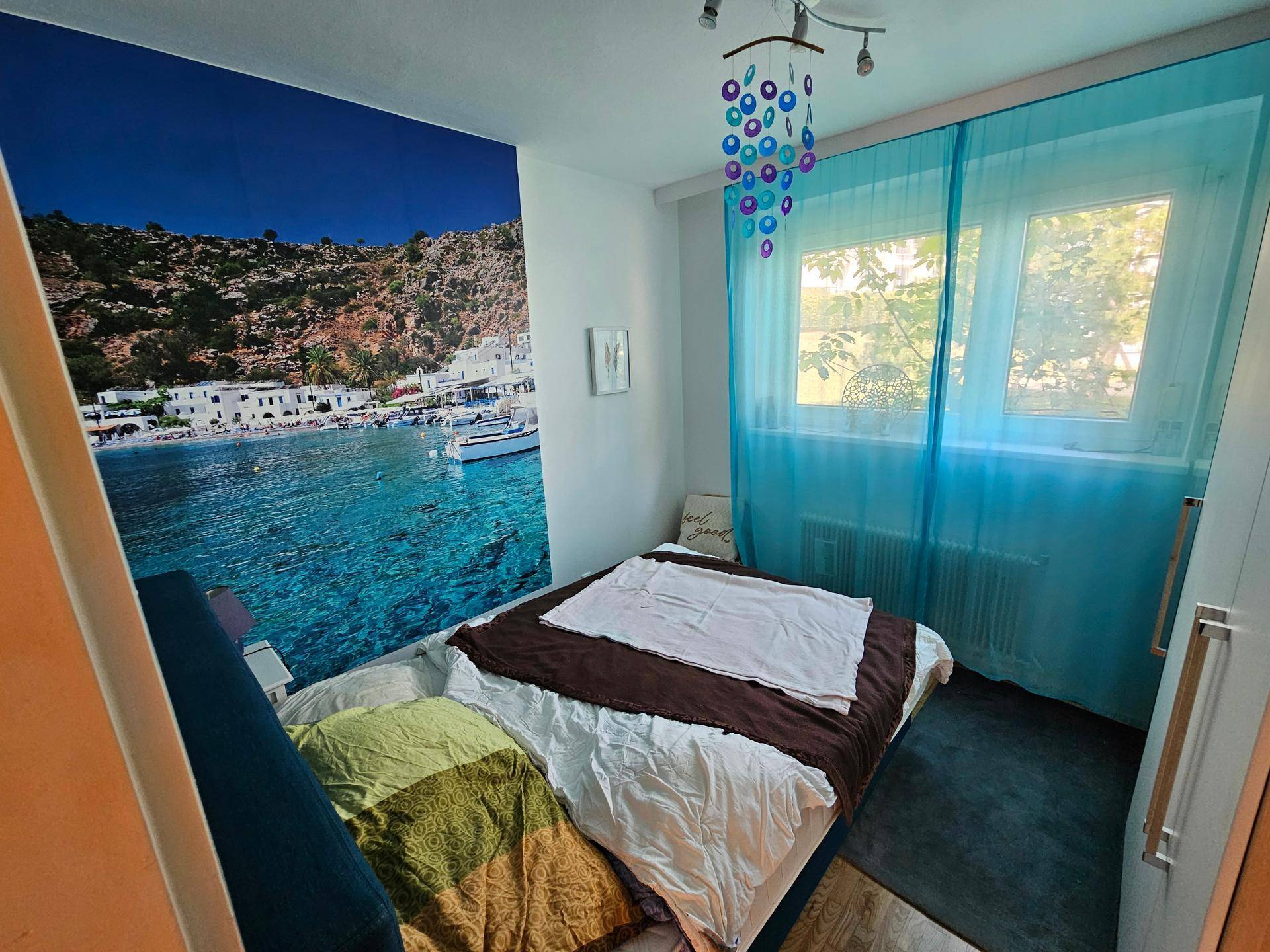 Schlafzimmer mit auffälliger Wandtapete, Doppelbett und blauen Vorhängen.