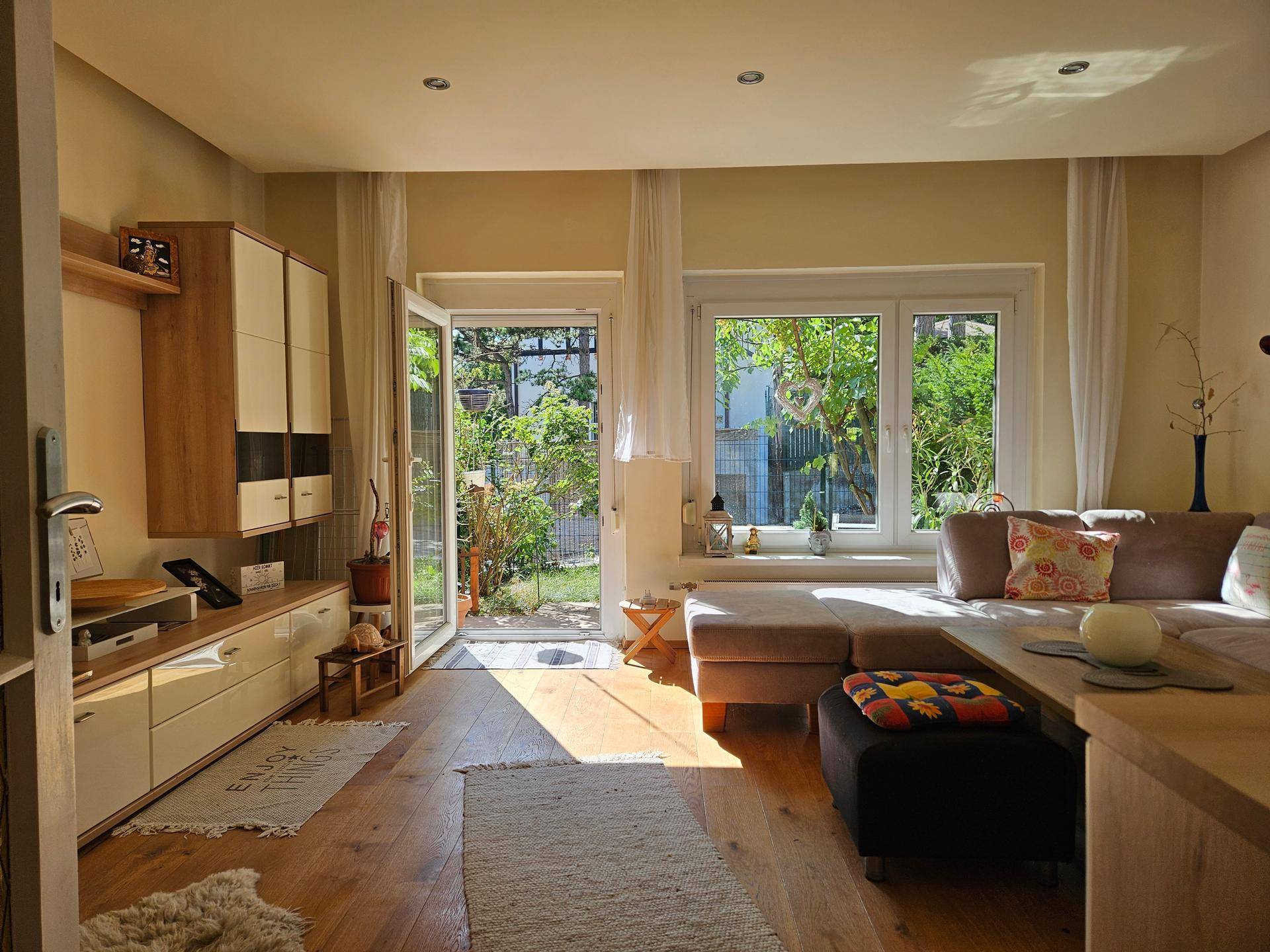 Helles Wohnzimmer mit Holzboden, großem Sofa und direktem Zugang zum Garten.