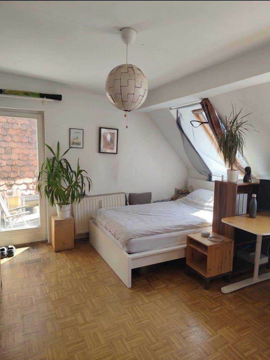 Helles Schlafzimmer mit Bett, Pflanzen und Zugang zu einem kleinen Balkon.