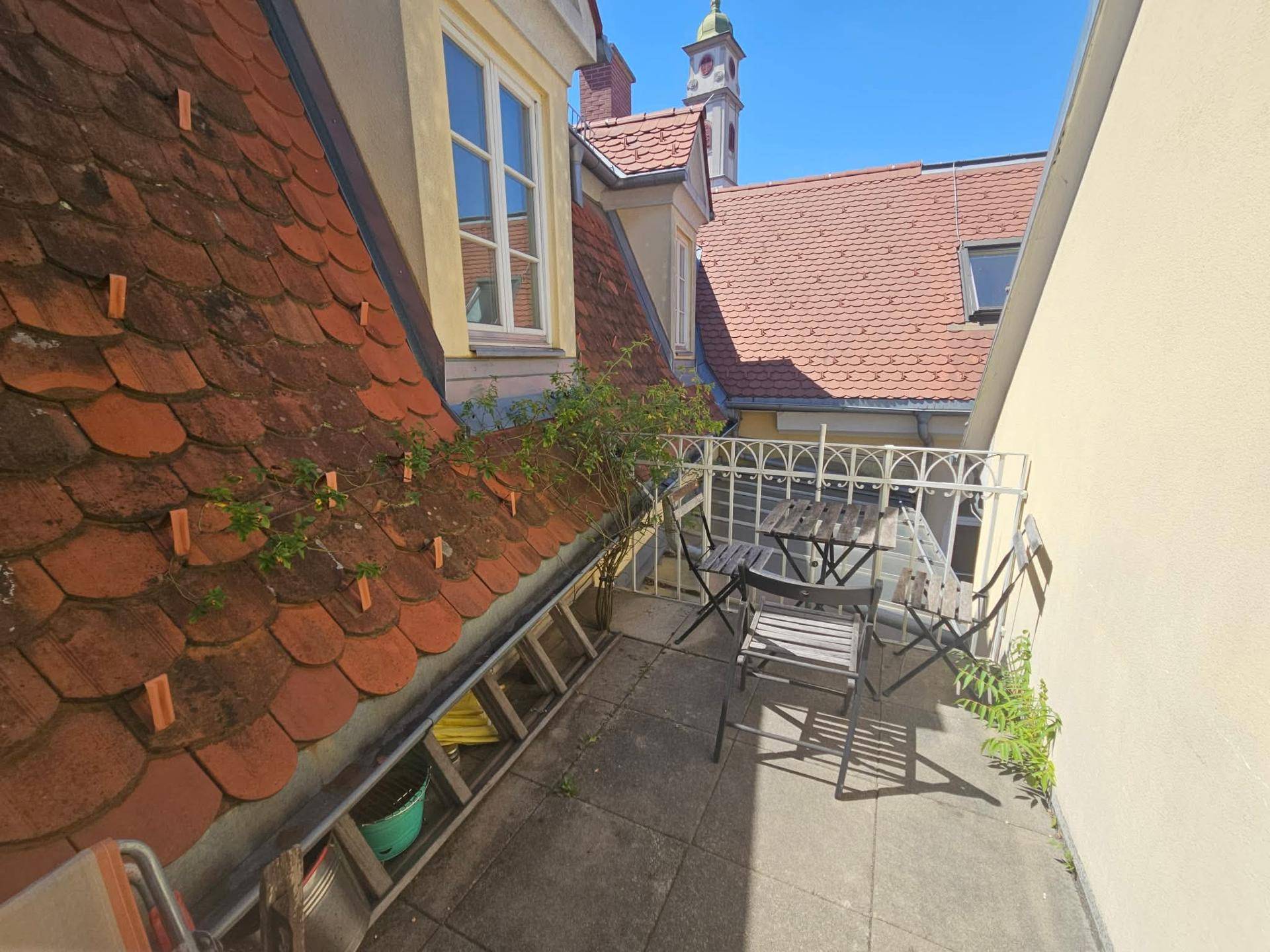Kleiner Balkon mit Sitzgelegenheiten und Blick über die Dächer und einen Kirchturm.