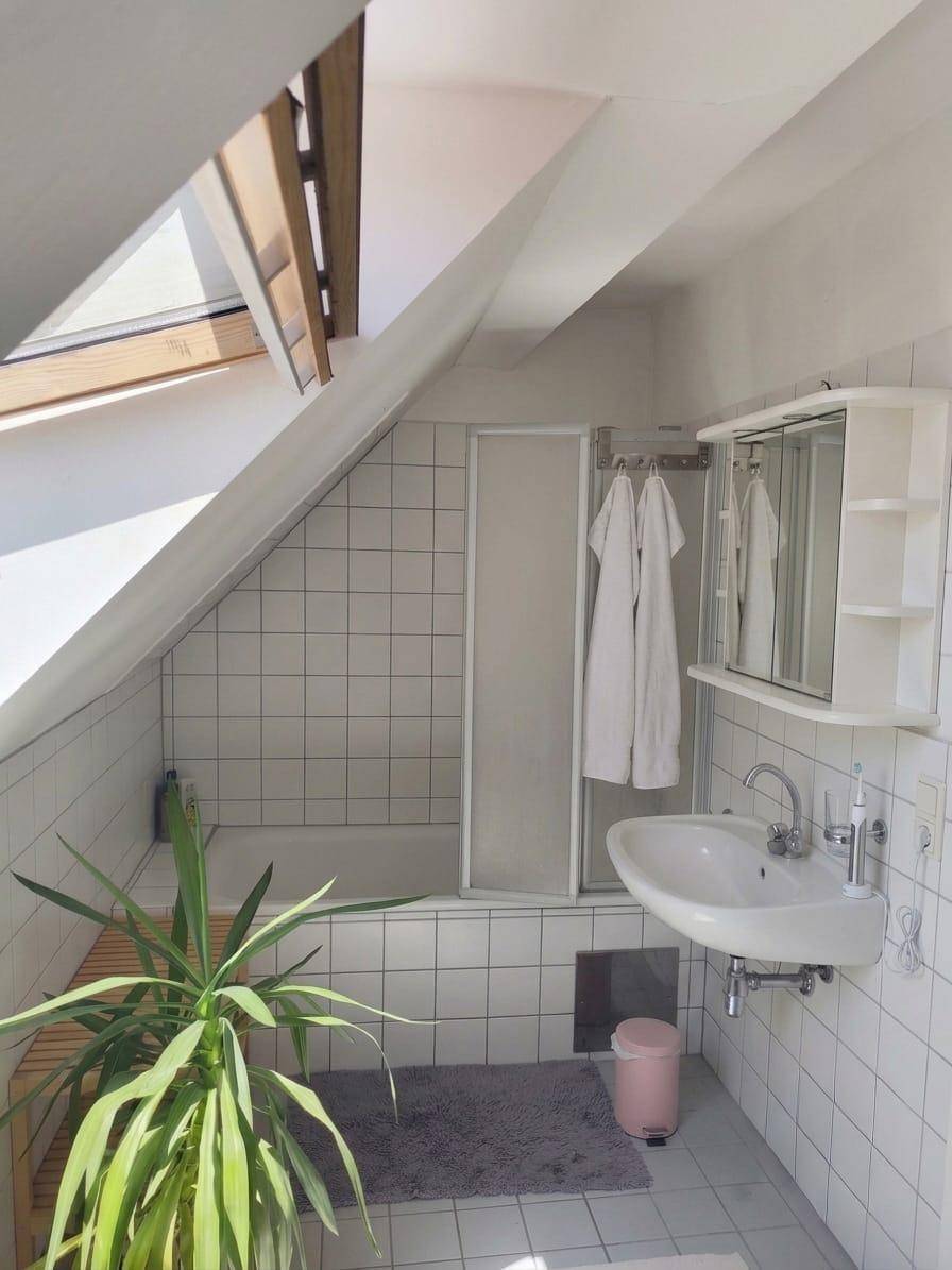 Helles Badezimmer im Dachgeschoss mit Badewanne, Waschbecken und Dachfenster.